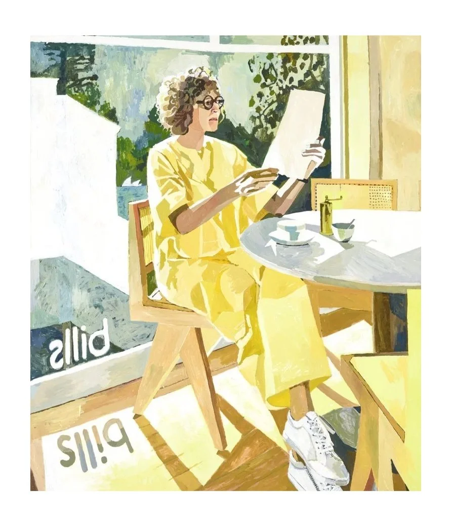 A woman with curly hair and glasses sitting at a table by a large window, reading a paper, wearing a yellow outfit, with breakfast items and a plant on the table.