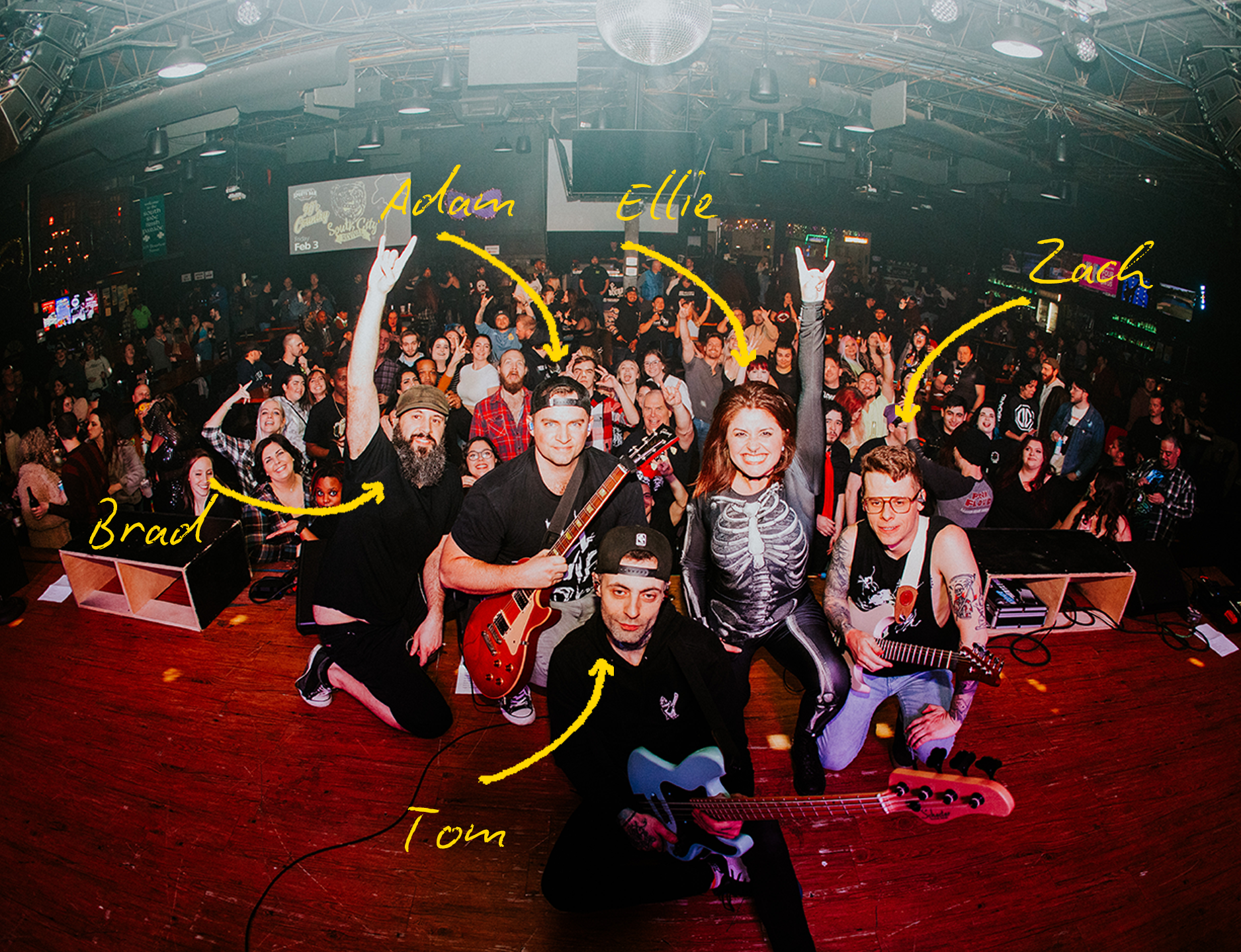 Photo of a band on stage with a crowd in the background. There are five band members labeled as Brad, Tom, Adam, Ellie, and Zach, holding guitars or standing on stage, with the audience cheering.