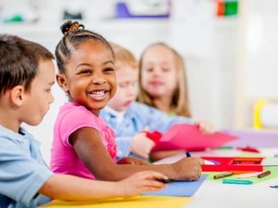 Smiling young girl in pink shirt with children in classroom.