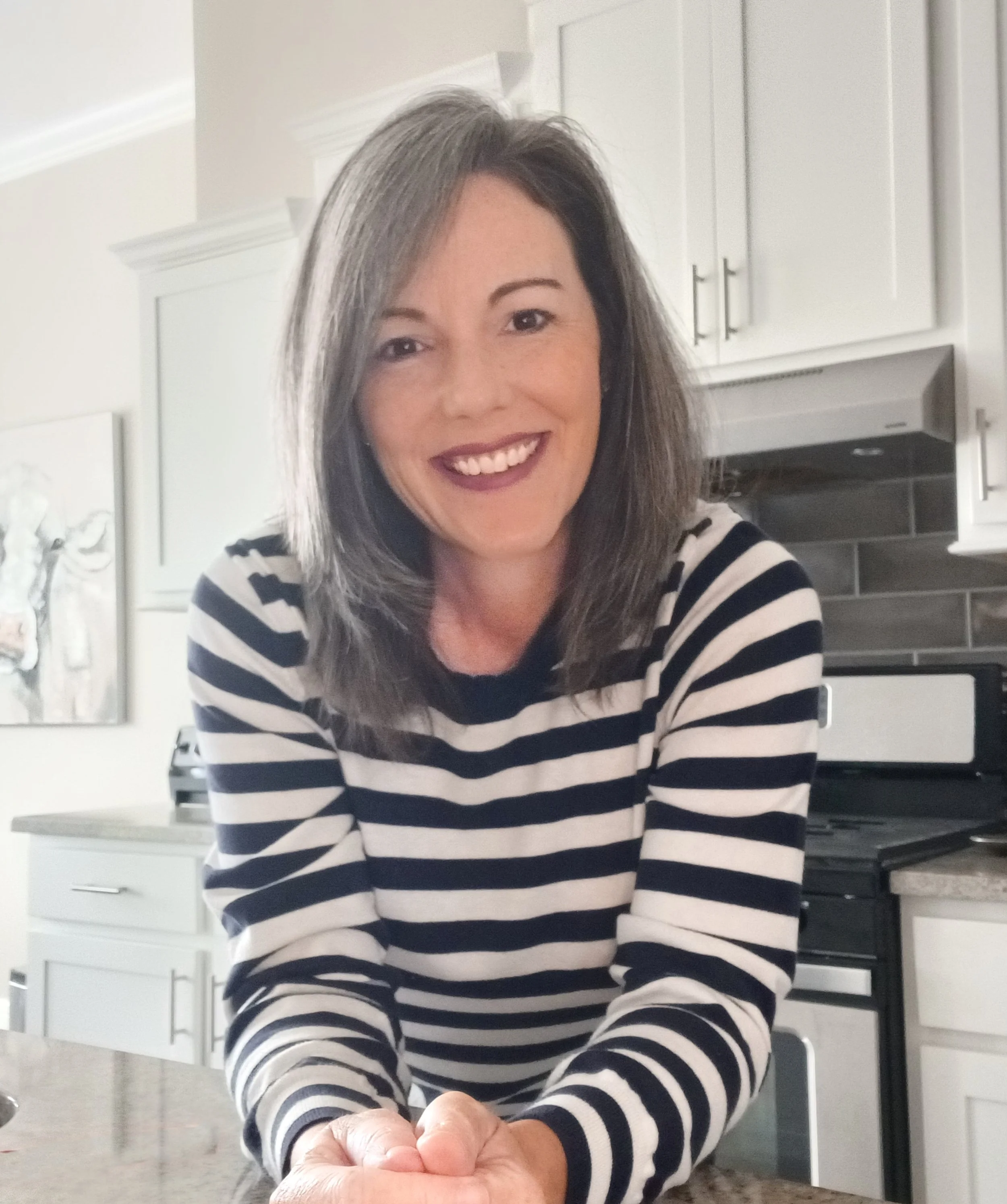Woman with gray hair in striped shirt smiling in a kitchen setting.