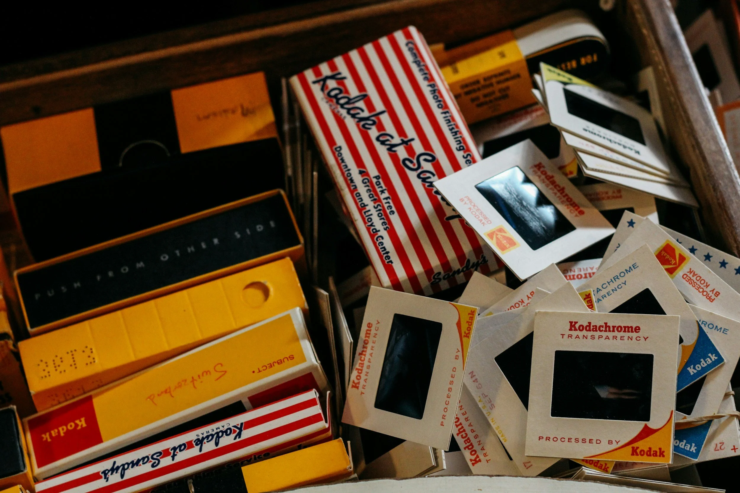 Collection of vintage Kodak film boxes and Kodachrome slides in a wooden drawer.