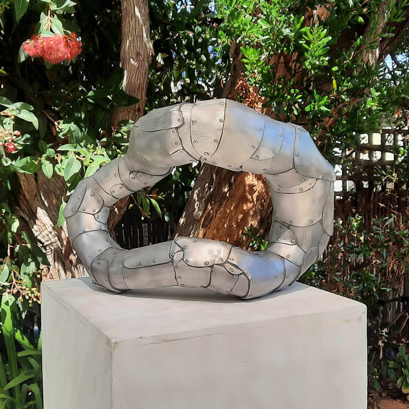 An aspect of a sculpture on a plinth in a garden made of riveted aluminium by Stephen Bond entitled Basic Loophole