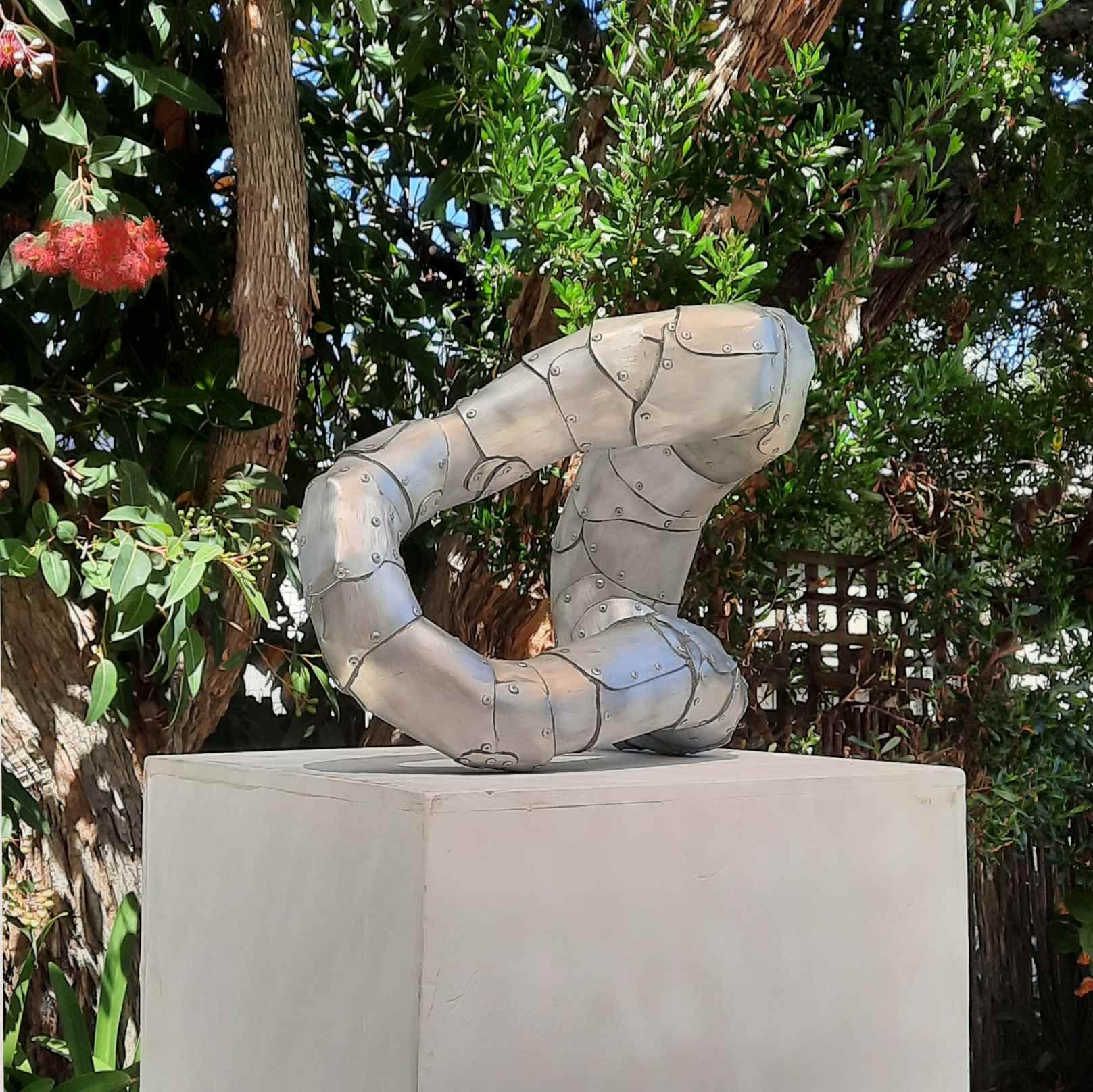 An aspect of a sculpture on a plinth in a garden made of riveted aluminium by Stephen Bond entitled Basic Loophole