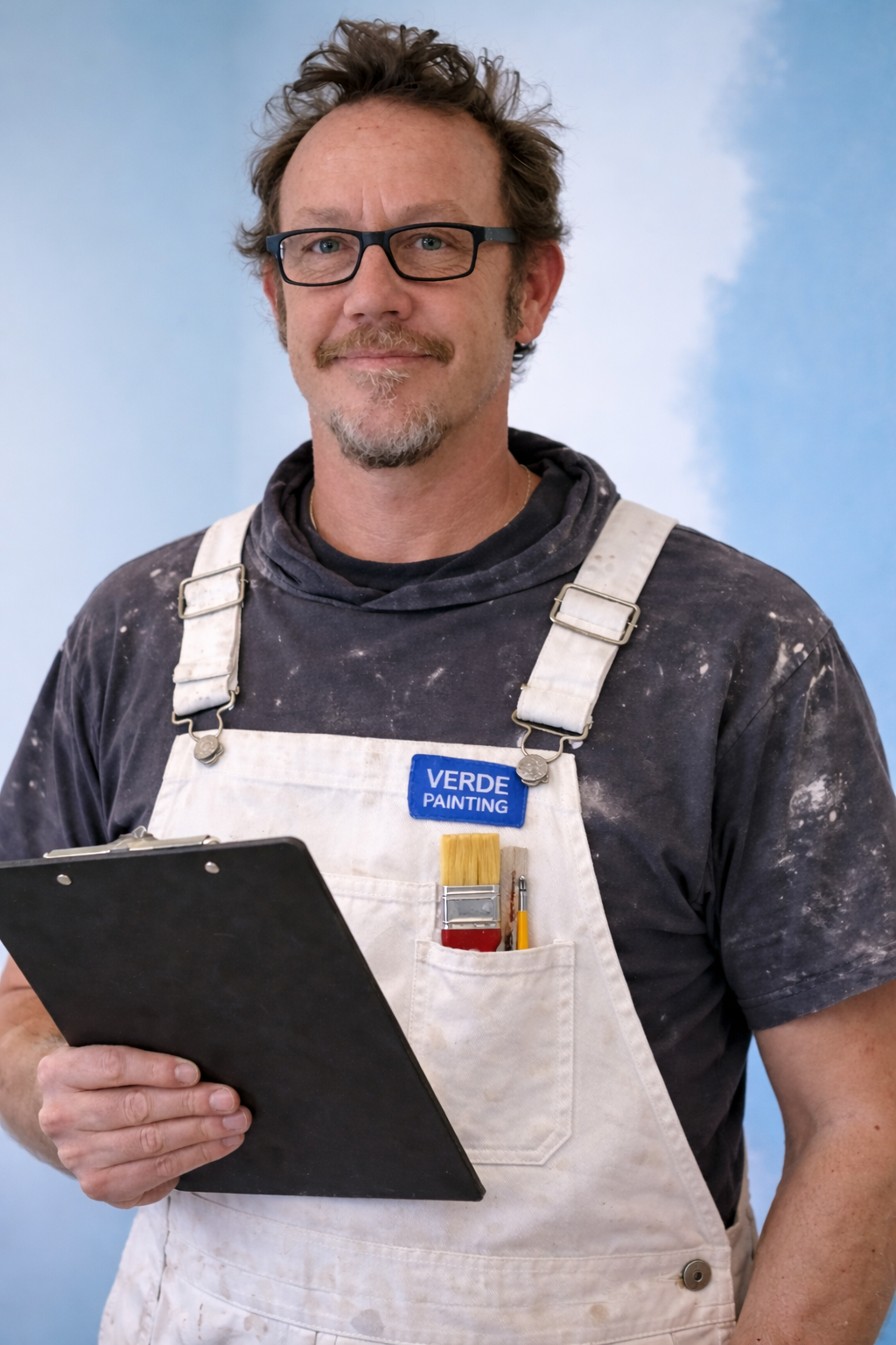 A man in a beige suit with a white shirt, sitting on a chair, with a neutral background.