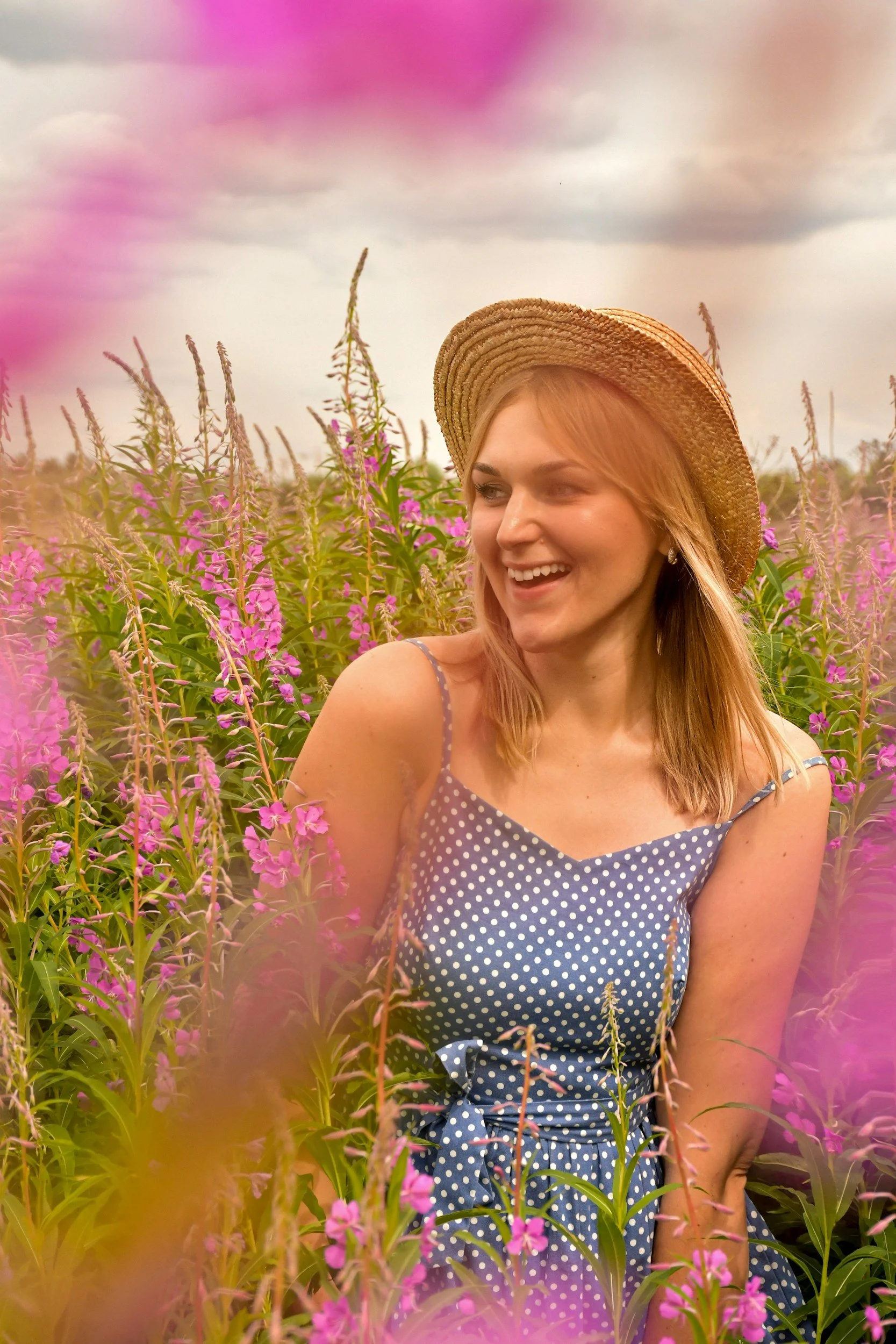 A smiling woman with a straw hat sits in a field of purple wildflowers represents the relief and joy that can come through Eating Disorder Treatment in Orlando, FL.
