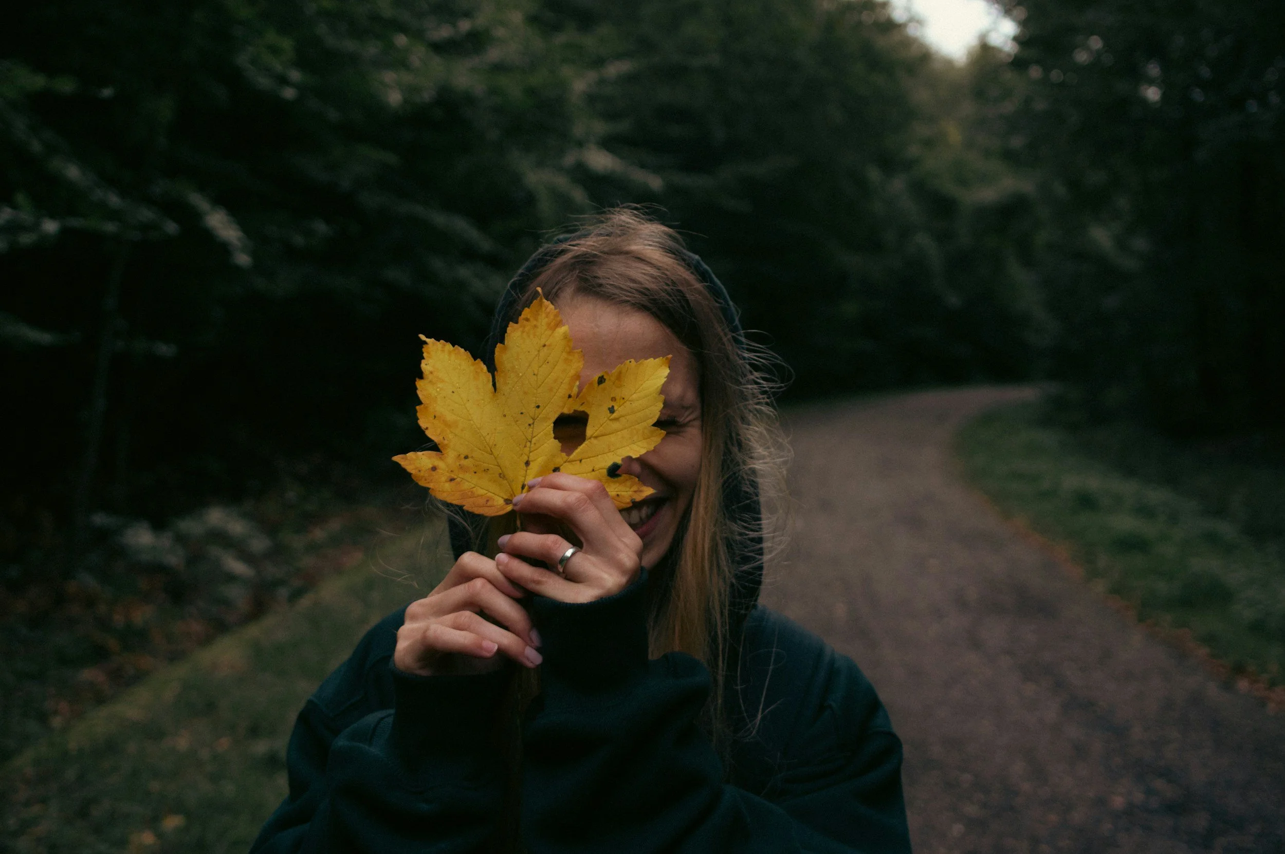 A smiling woman holds a fall leaf in front of her face as she celebrates persevering through the fall season with the help of an Eating Disorder Therapist in Orlando, FL.