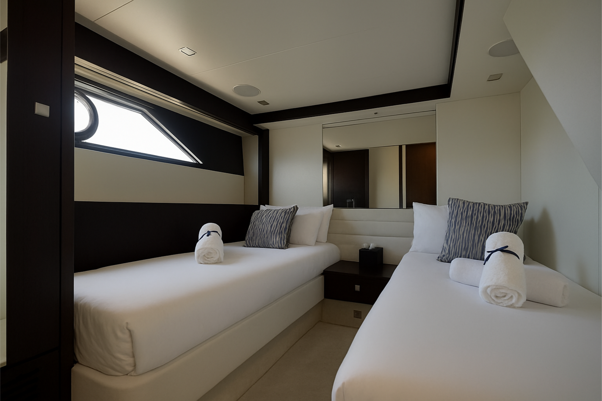 Two twin beds with white bedding, rolled towels, and decorative pillows in a modern room with a large window and a mirror.
