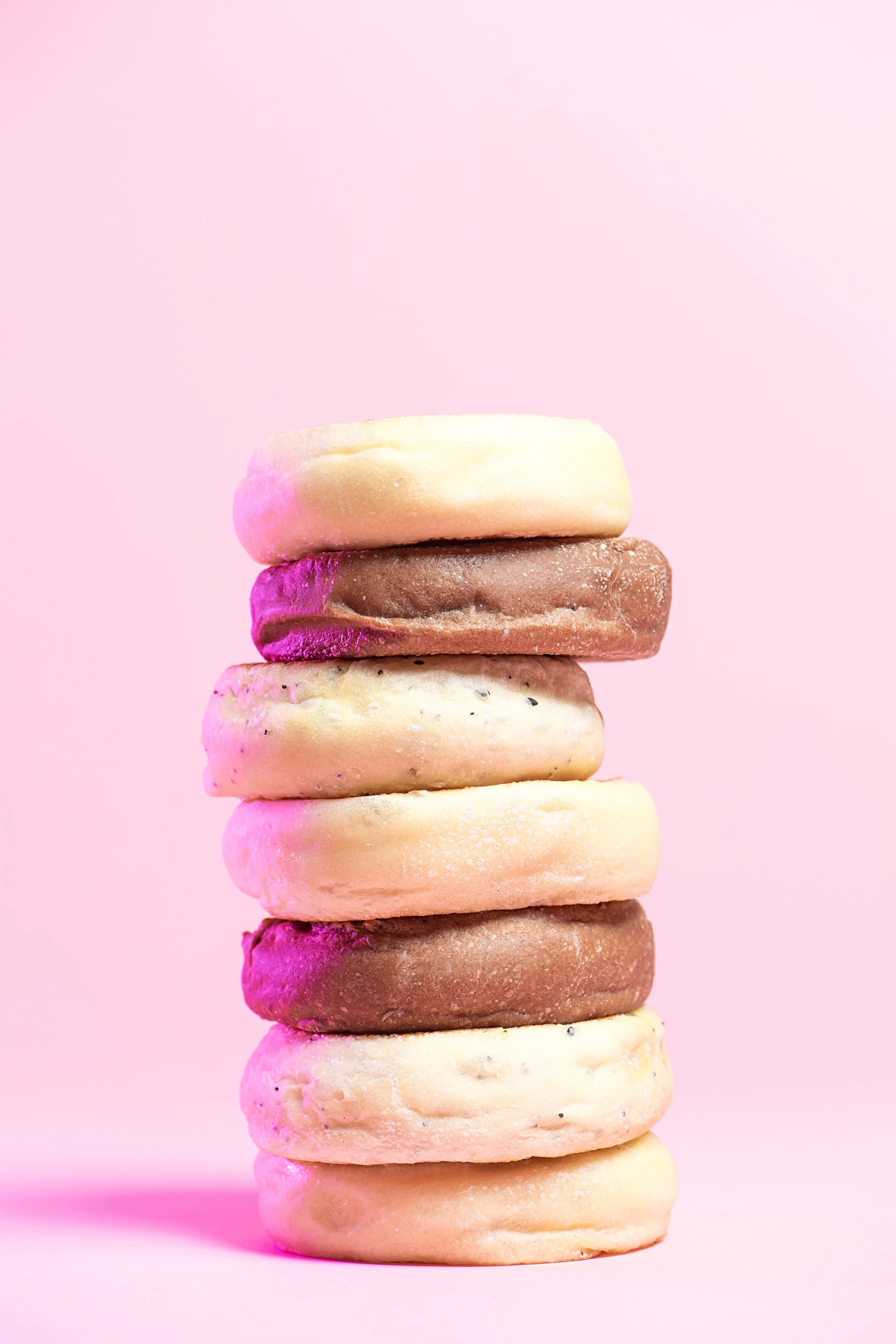 A tall stack of colorful donuts with pink, brown, and white icing against a pink background.