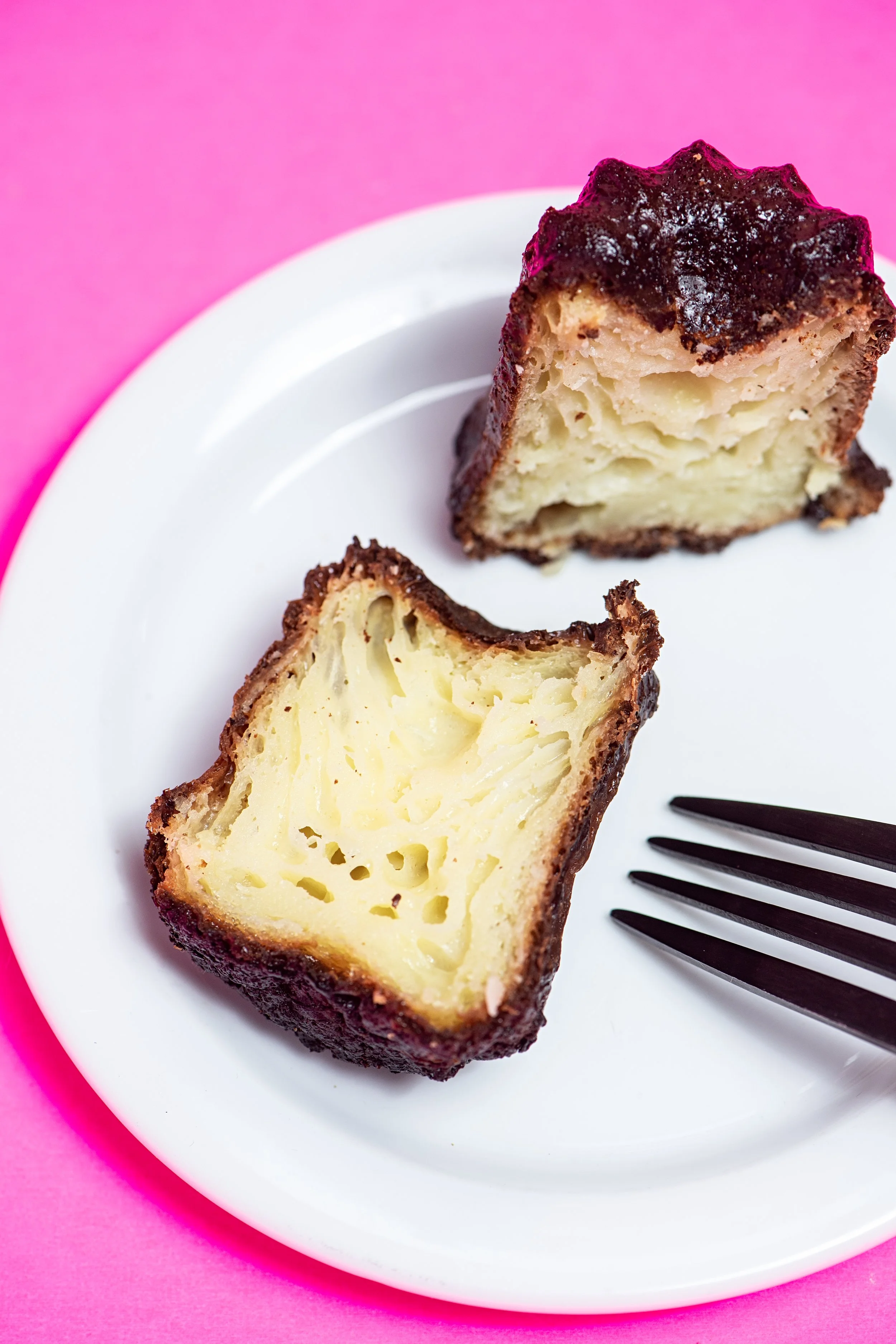 A slice of baked cheesecake on a white plate, with a fork beside it, against a pink background.