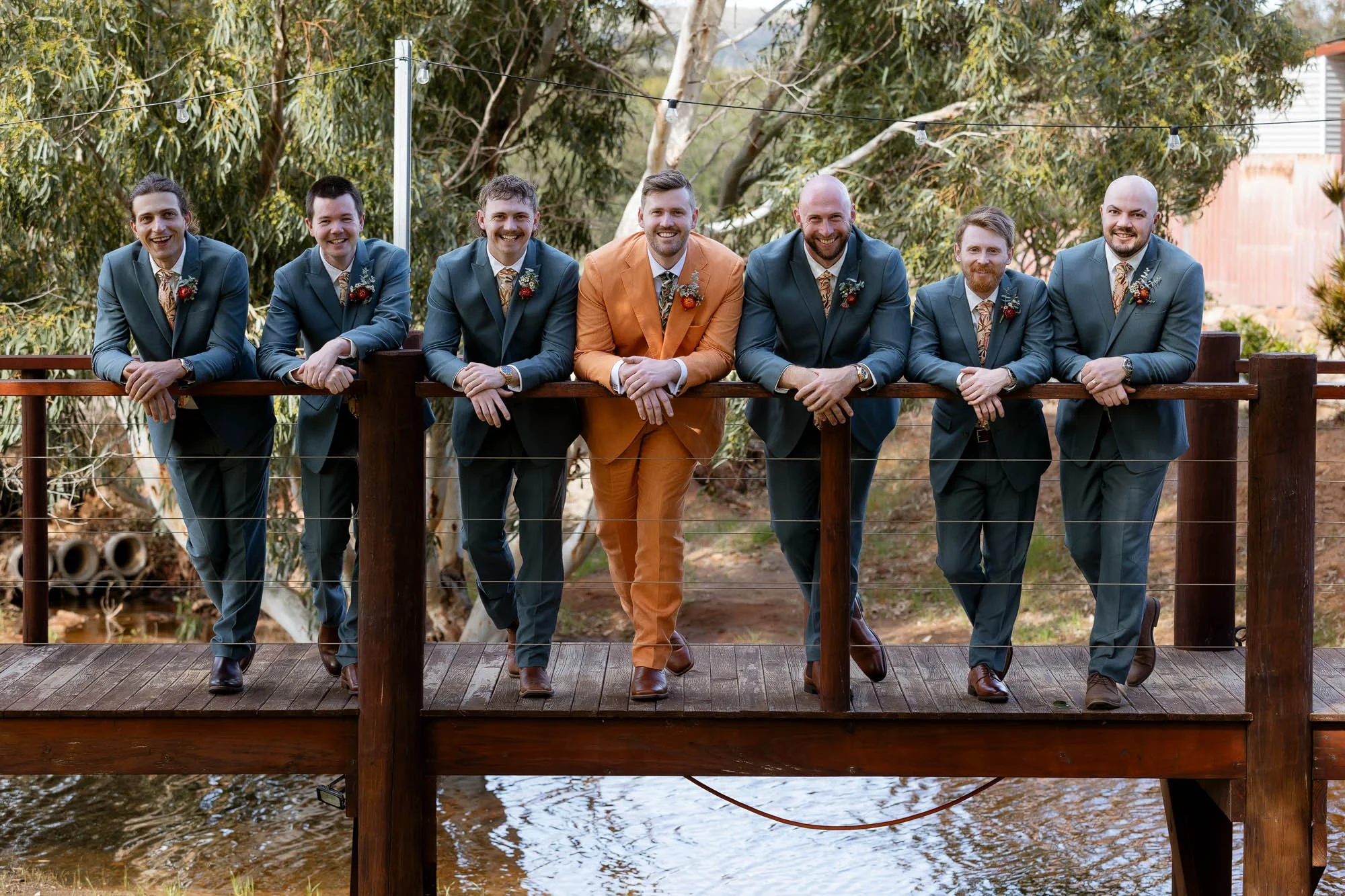 Groom and Groomsmen leaning on railing on bridge looking at camera