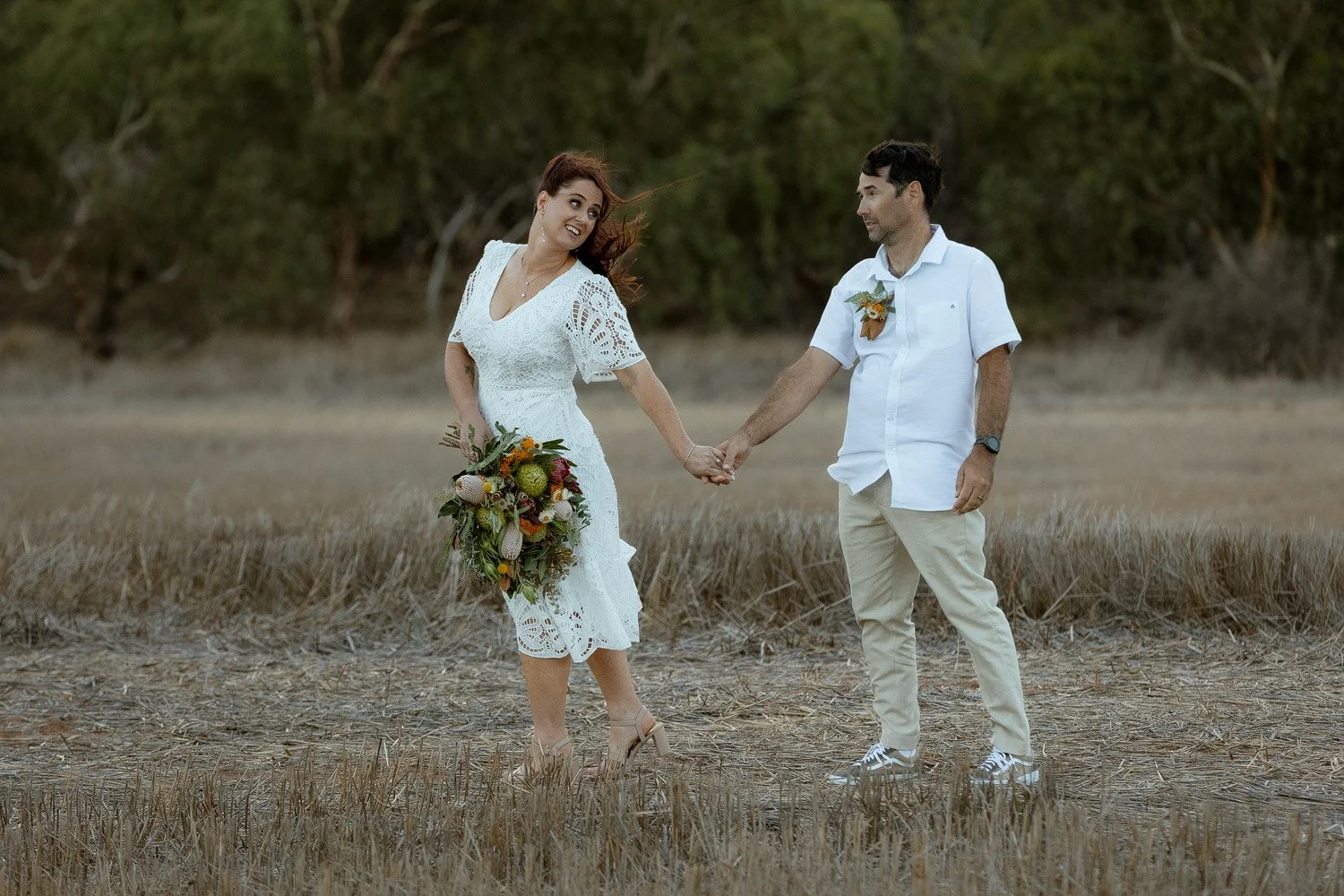Bride leading Groom walking hand in hand in paddock 