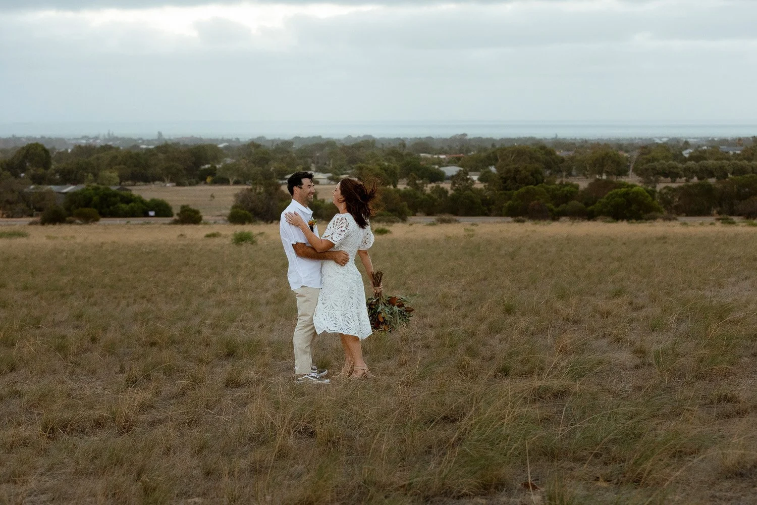 Bride and Groom embrace over looking the ocean on a hill 