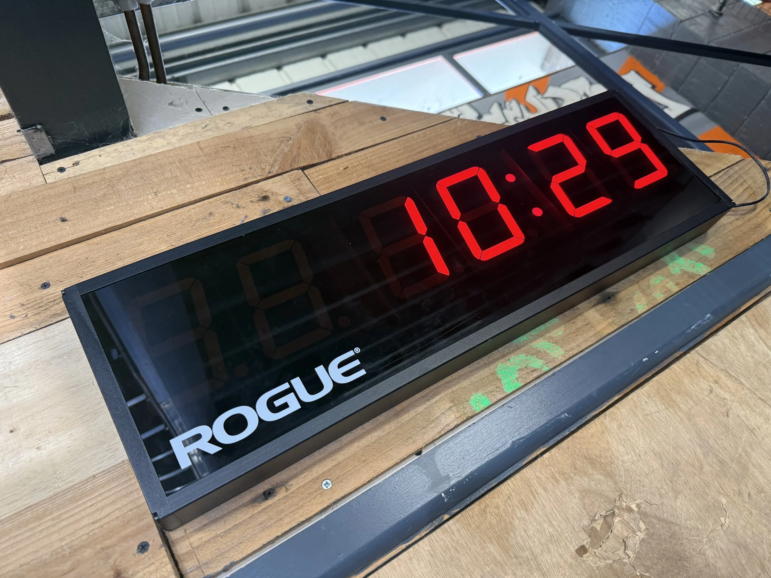 Digital timer displaying 10:23 placed on wooden surface with part of a sign reading 'ROGUE' visible.