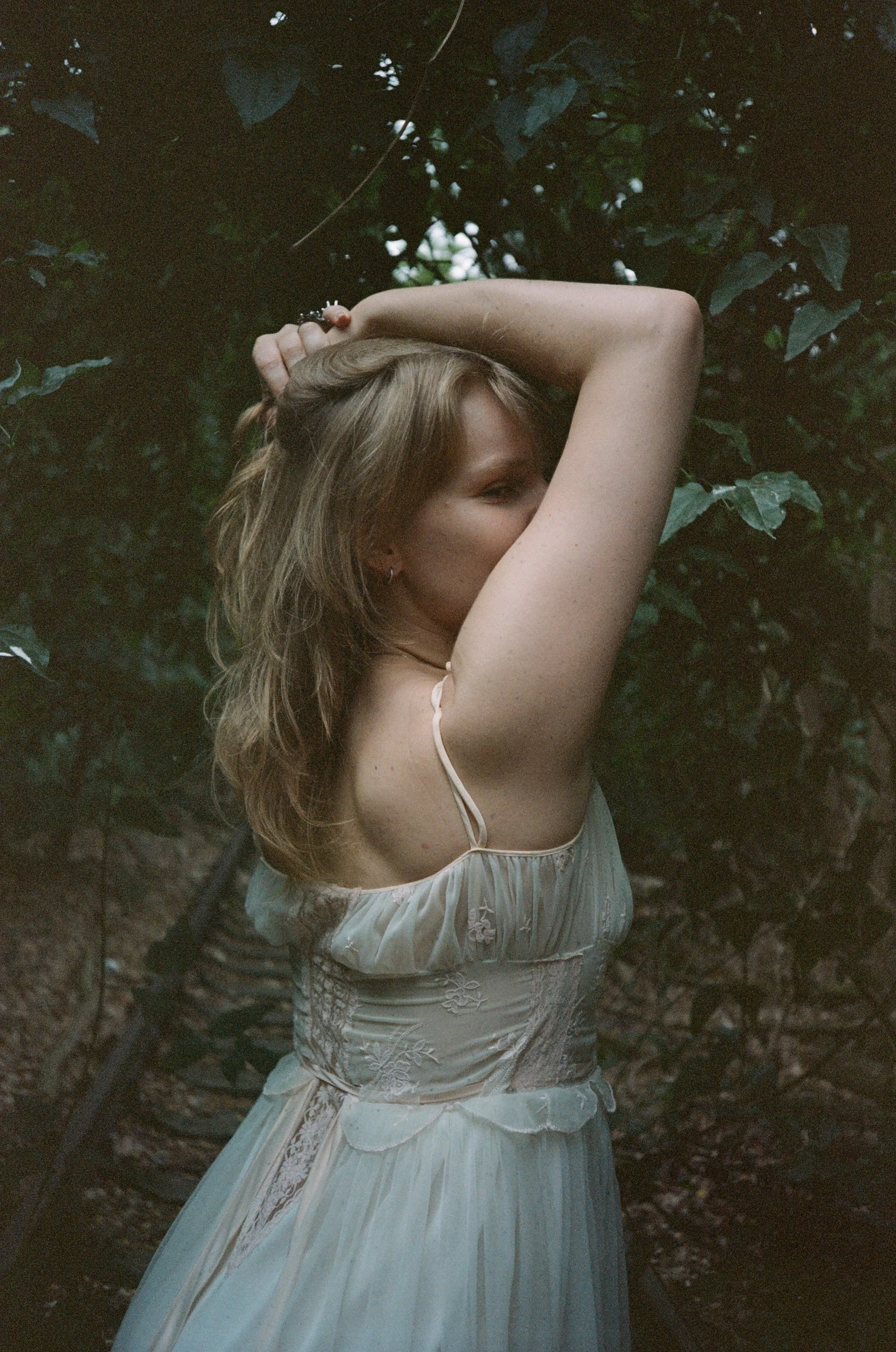 Luxury Berlin Escort Lyra Bergman poses in a vintage lingerie dress in the forest by the train tracks; softly lit analogue image taken by @filminale_