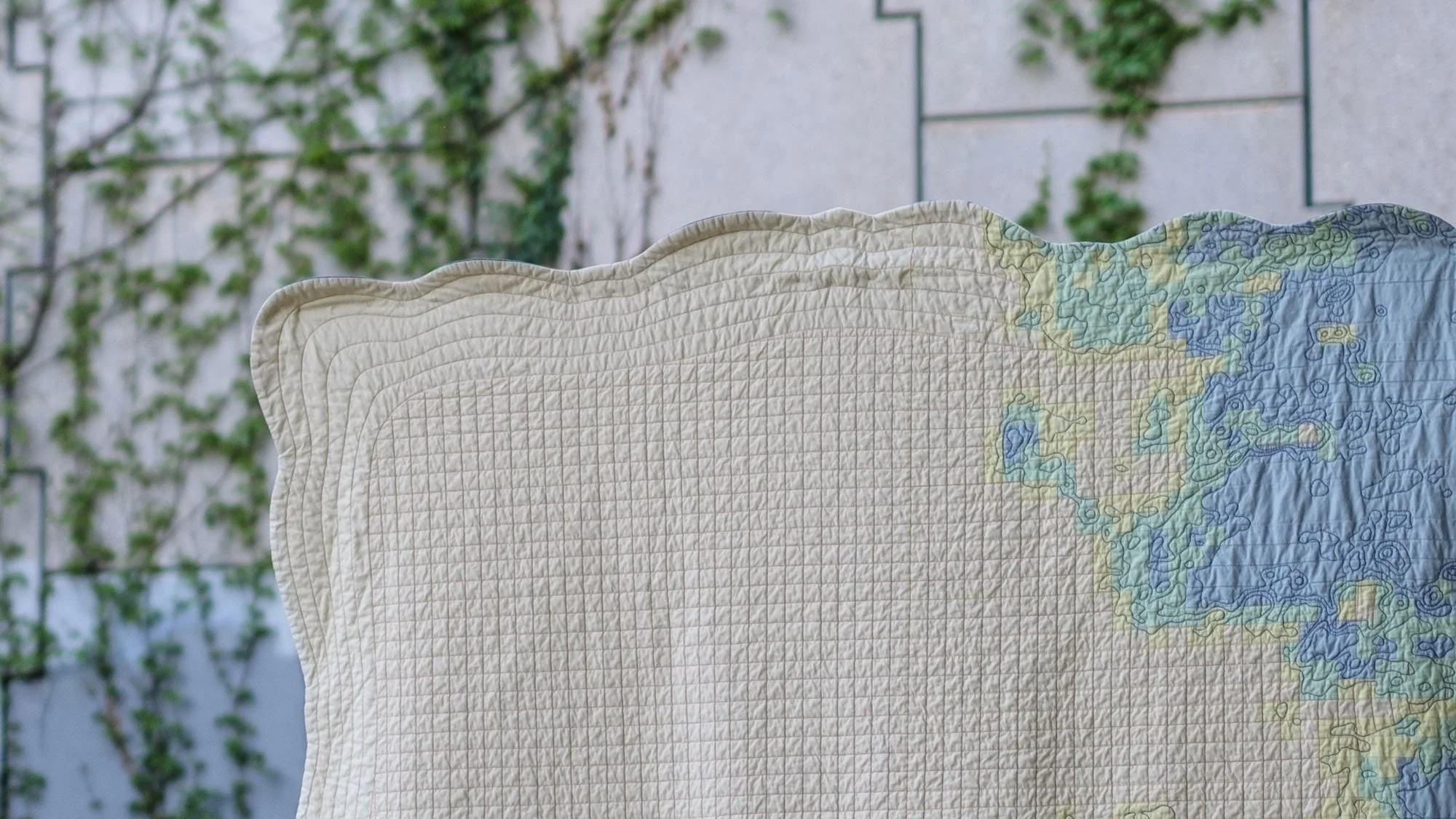 Top third of the quilt showing the curved frame edge transitioning into blue and green pieced forms.