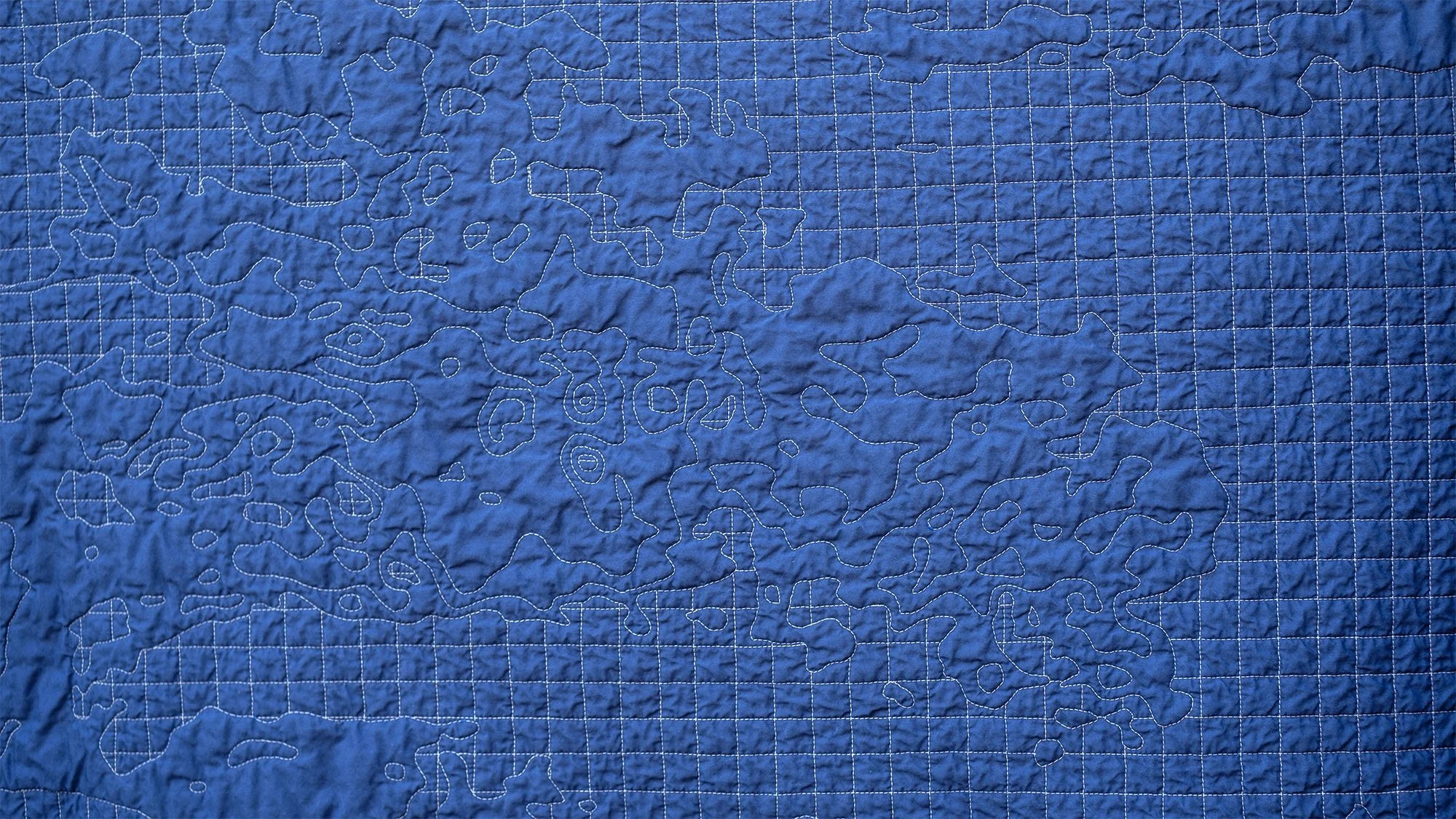 Close-up of the blue quilt back showing stitched contour shapes interrupting a uniform quilted grid.