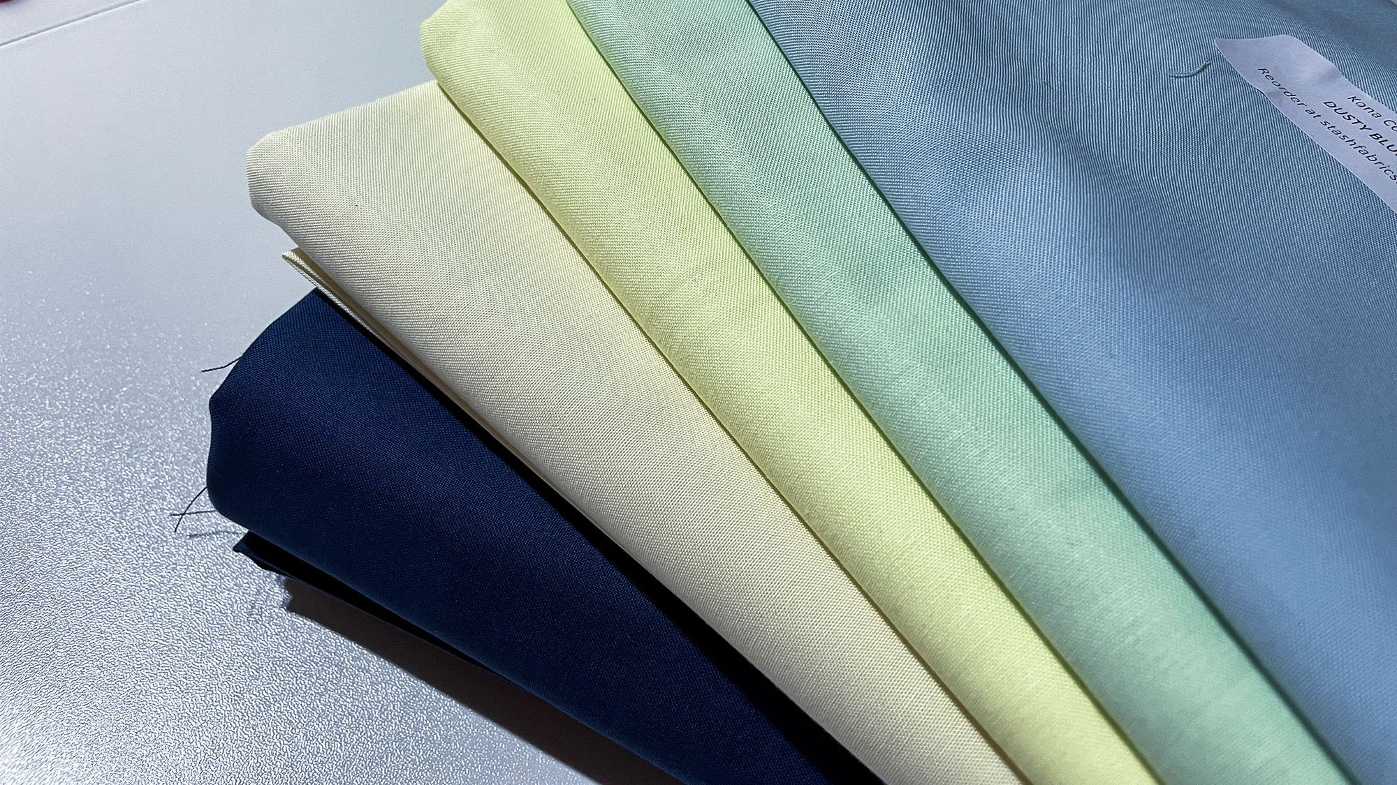 Stack of selected fabrics in pale blue, mint, cream, and deep royal blue used throughout the quilt.