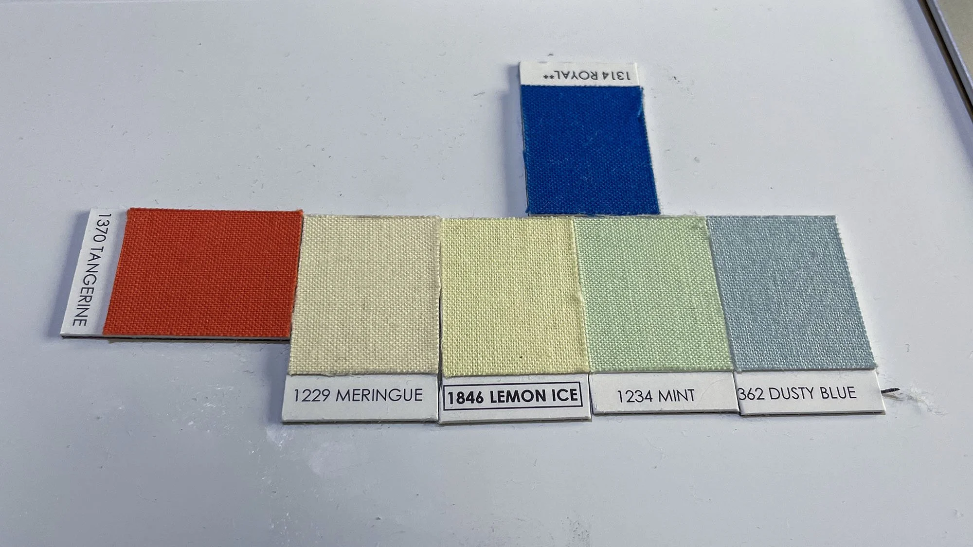 Fabric swatches used to plan the quilt color palette, including bright red and saturated blue accent colors alongside pale greens and blues.
