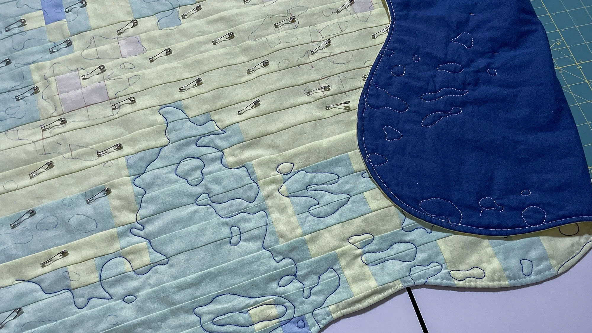 Quilt in progress with safety pins basting the layers together and contour quilting stitched near the curved border.