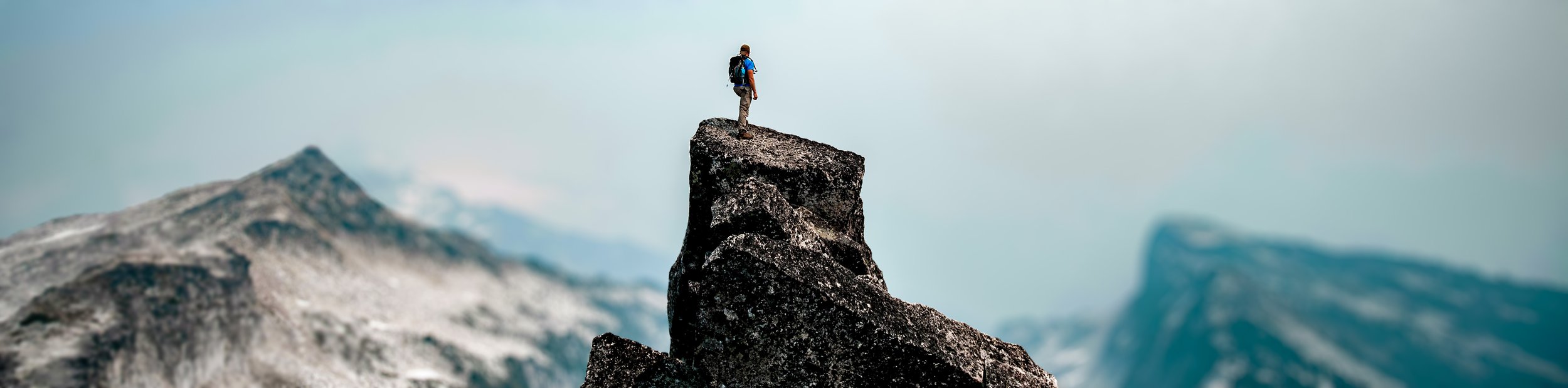 man standing on mountain top with blue sky, surrounded by other cliff tops signifying success