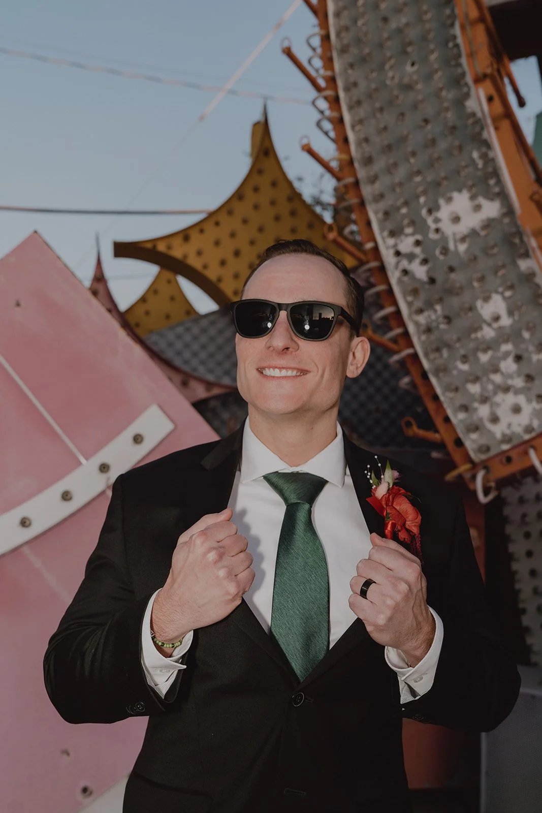 Portrait of the groom adjusting his jacket while standing among vintage neon signs at the Neon Museum.