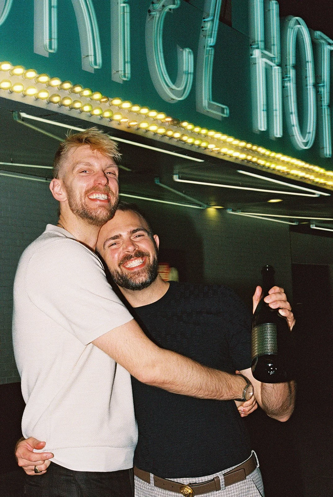 Couple smiling at the camera with a bottle of champagne during their Fremont Street elopement in Las Vegas on 35mm film.