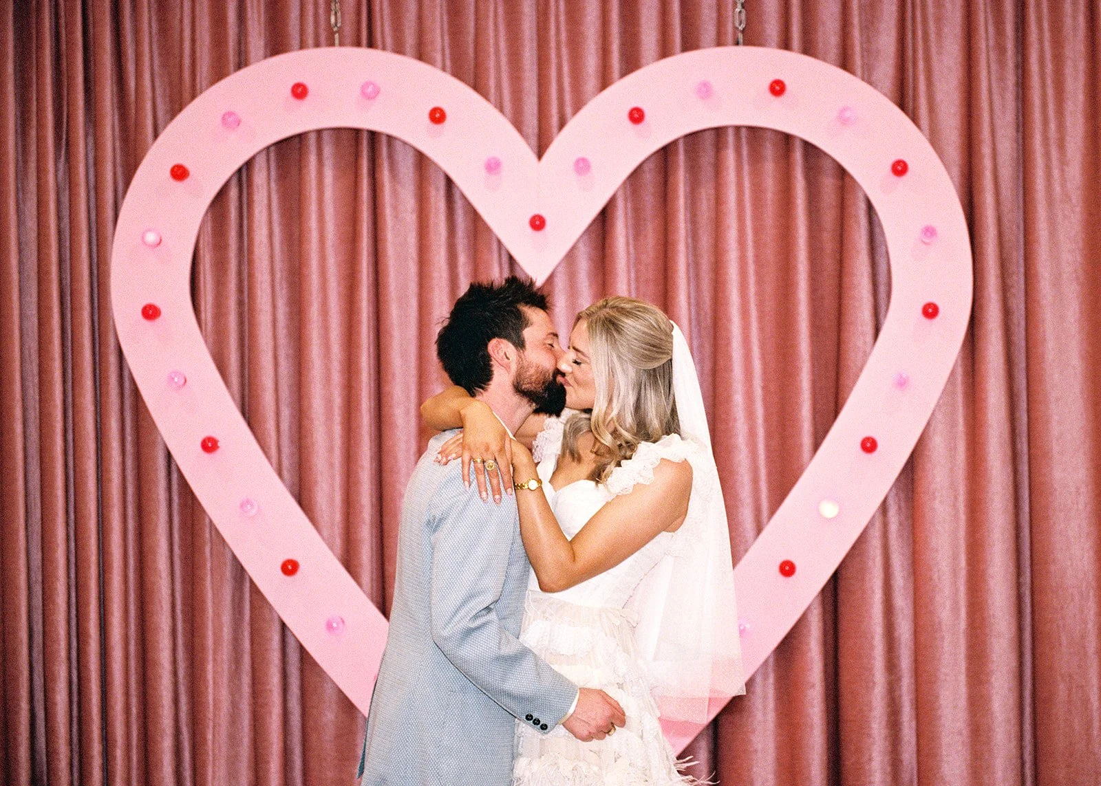 Bride and groom kissing in front of the pink heart at Sure Thing Chapel on 35mm film.