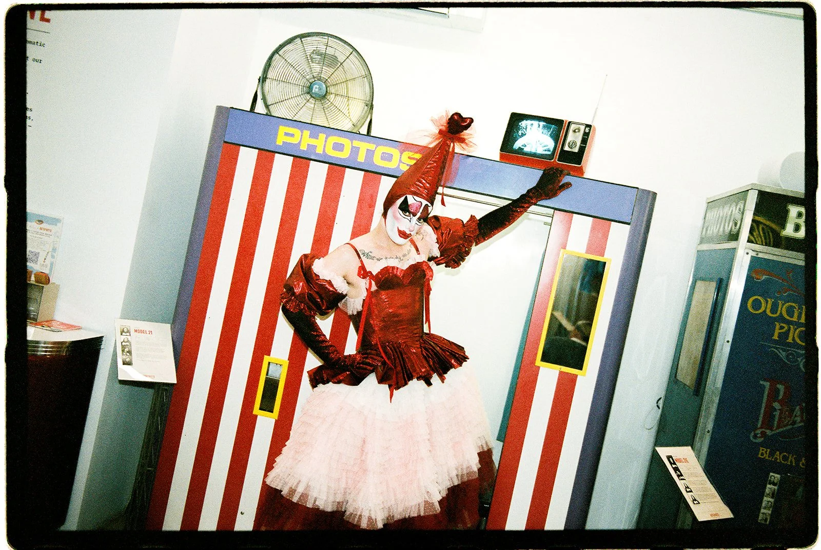 Tillie the Clown standing beside a vintage red-and-white striped photobooth at the AUTOPHOTO Museum in NYC.