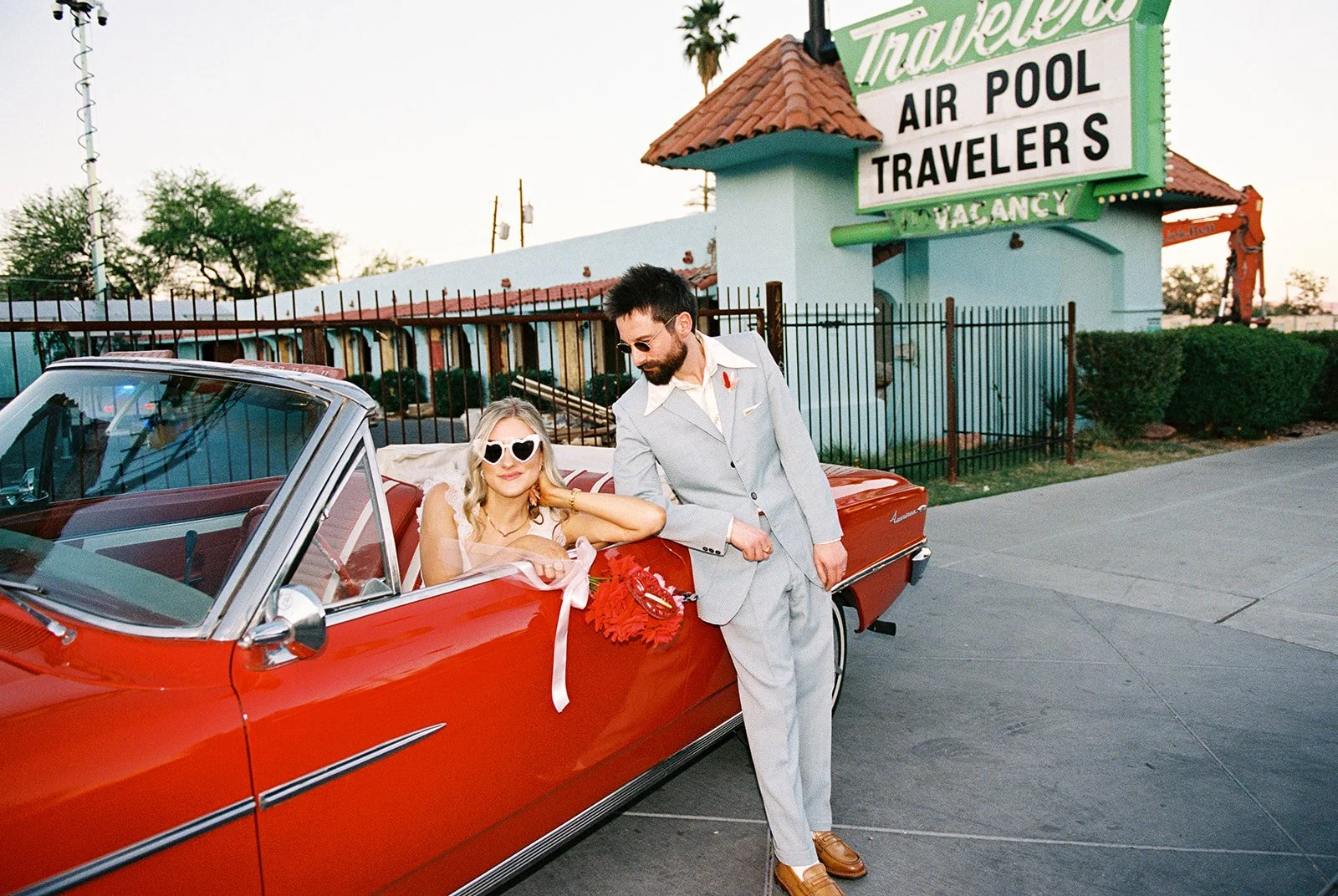 Bride and groom posing with the red convertible in front of Travelers Motel in Las Vegas.