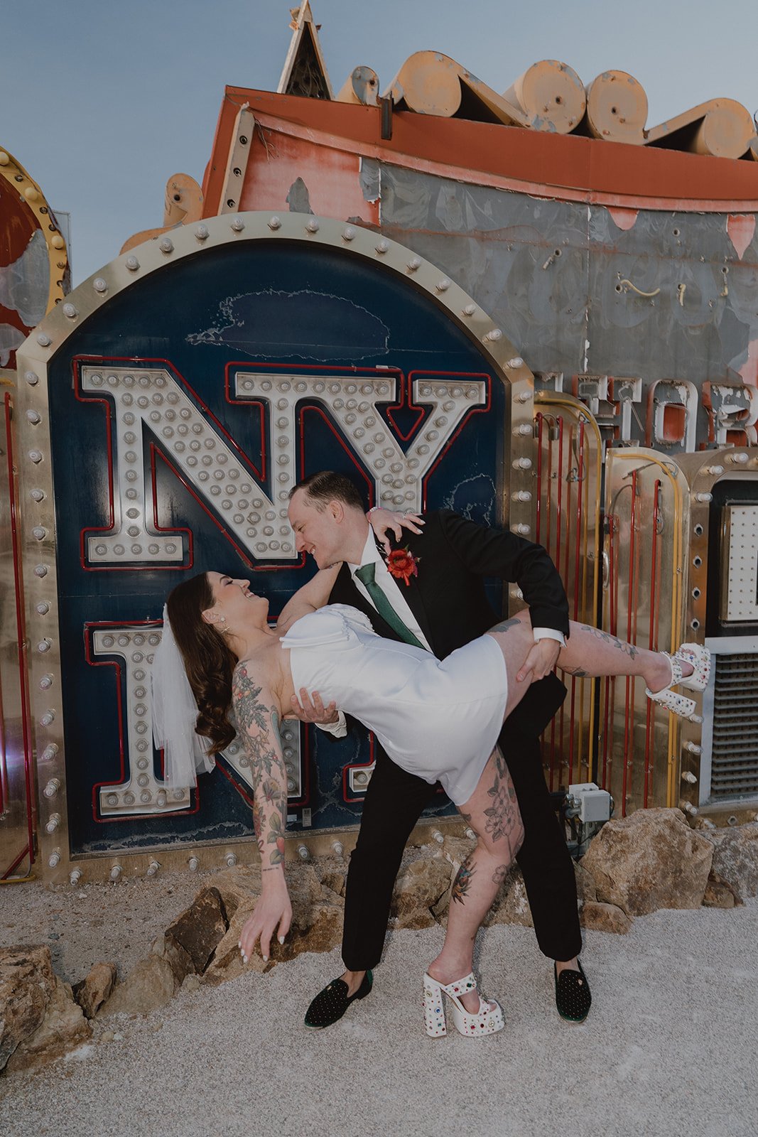 Groom lifting the bride in front of a large NY neon sign in the North Gallery at the Neon Museum.