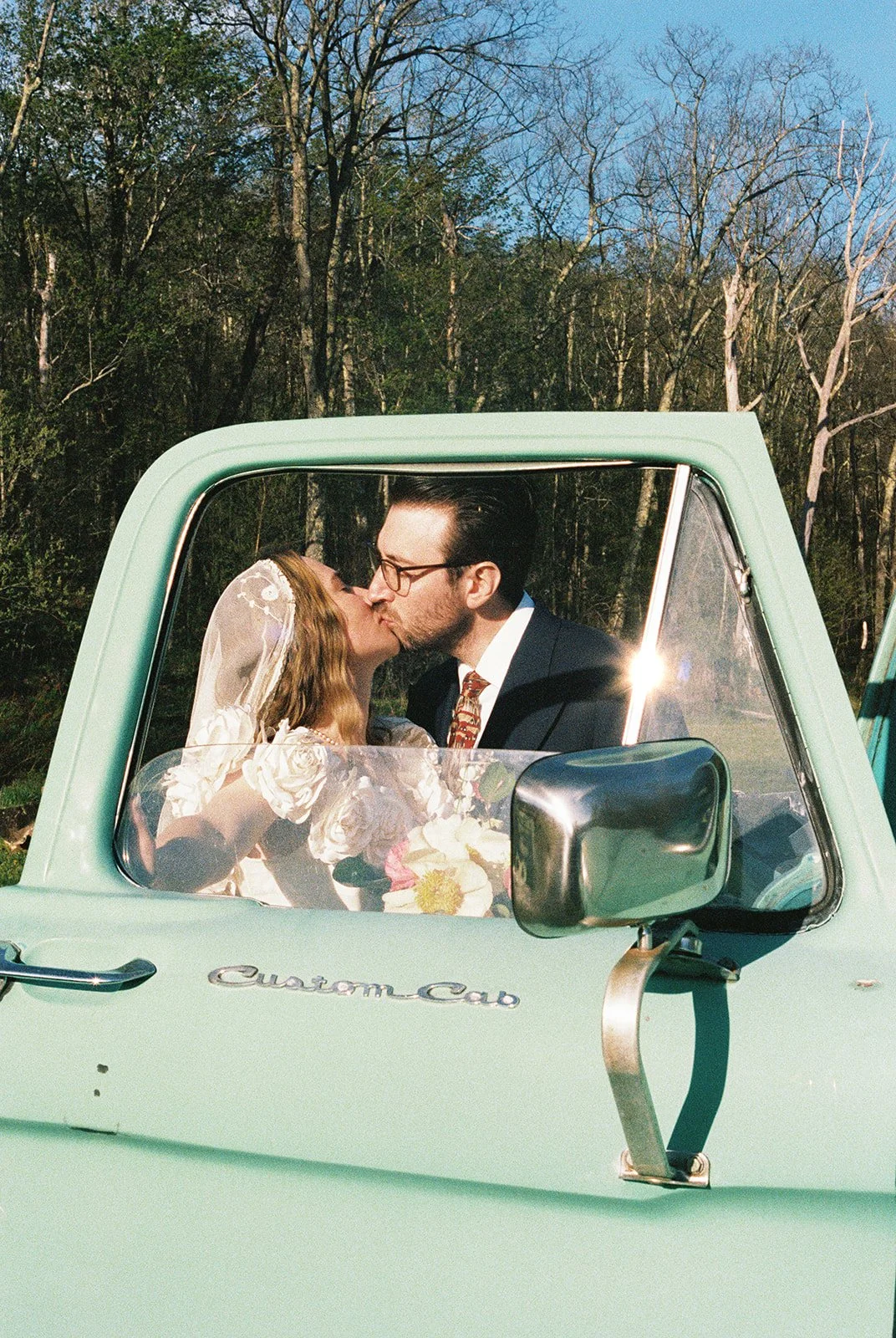 Bride and groom kissing behind the window of a vintage green truck.