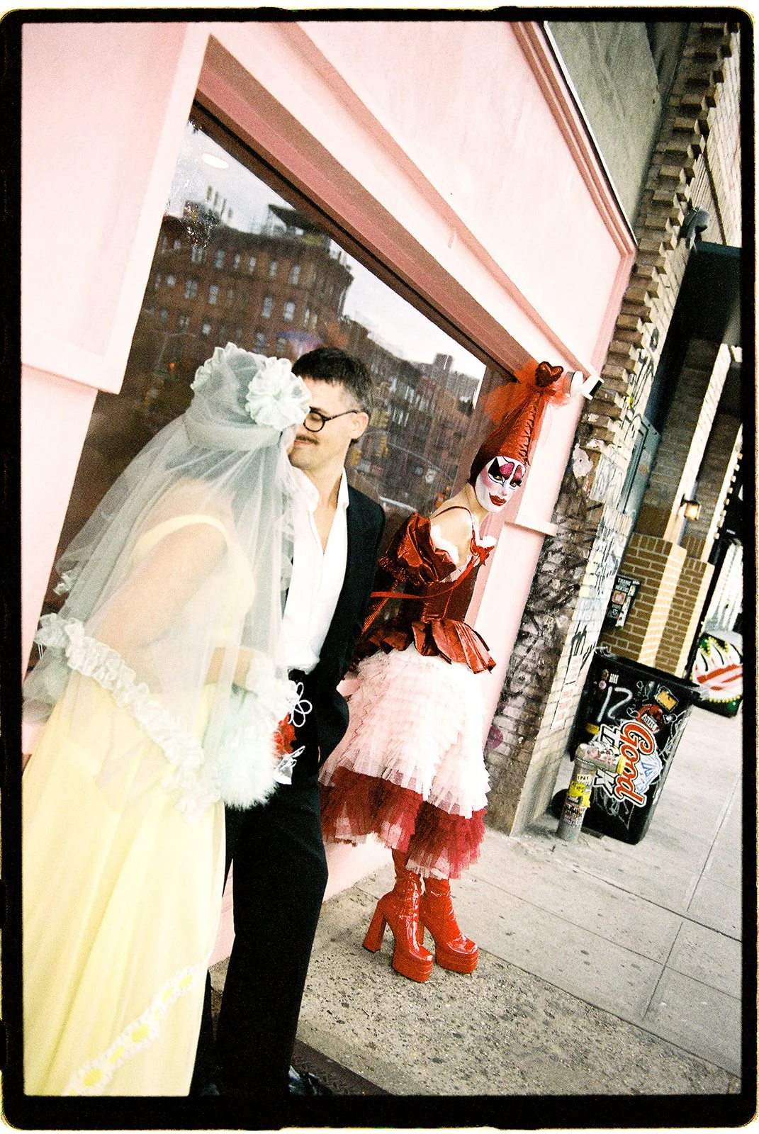 Couple sharing a moment outside Sure Thing NYC with Tillie the Clown standing near the chapel's pink exterior.