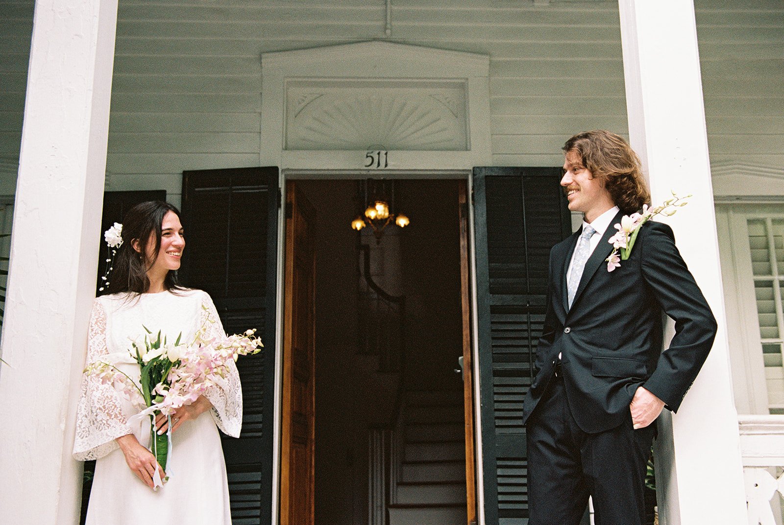 Bride and groom laughing together on the porch surrounded by palms during their Key West Florida elopement.