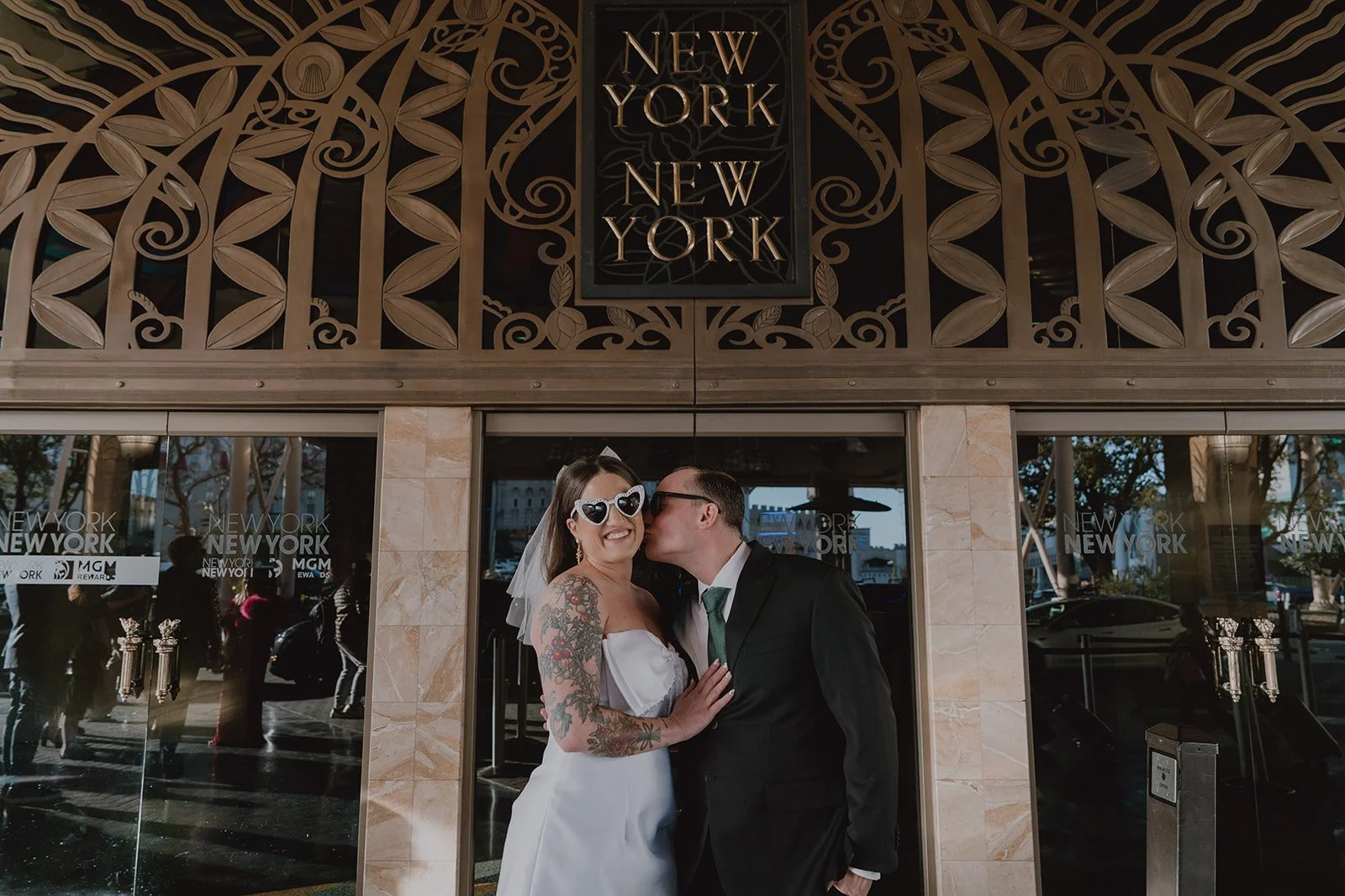 Groom kissing the bride on the cheek while posing outside of New York New York Hotel Casino in Las Vegas.