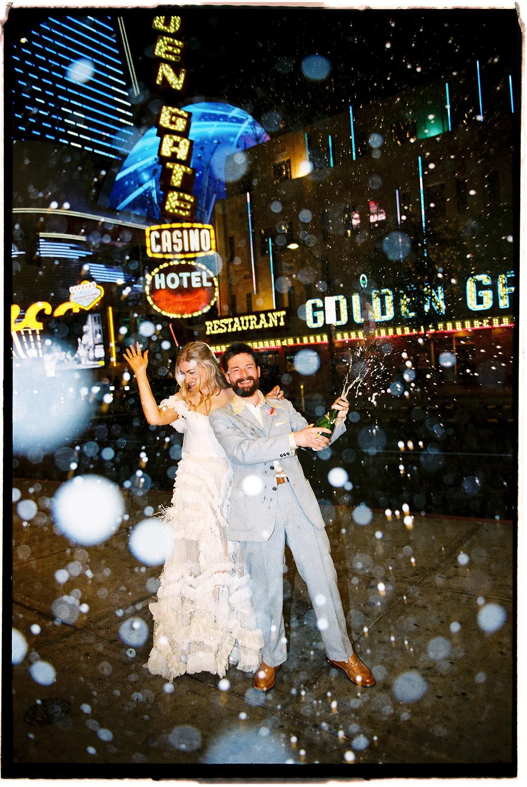 35mm film photo of a bride and groom popping champagne on Fremont Street in front of Golden Gate Casino & Hotel.