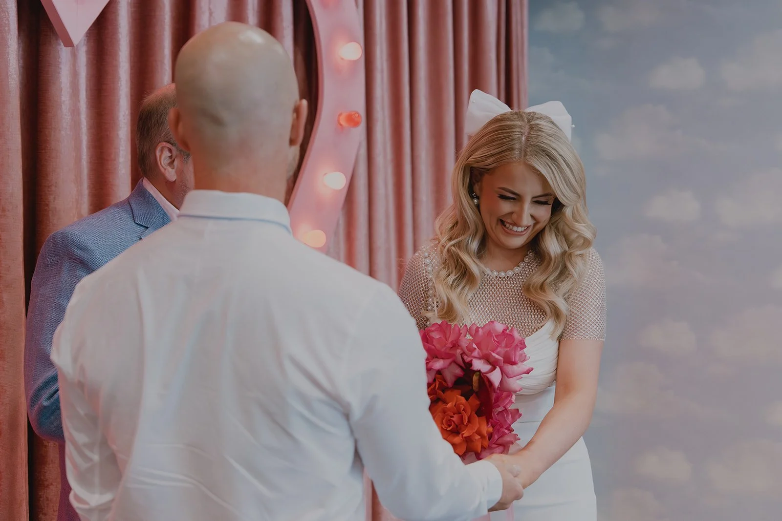 Bride smiling during vows at Sure Thing Chapel with pink velvet curtains behind her.