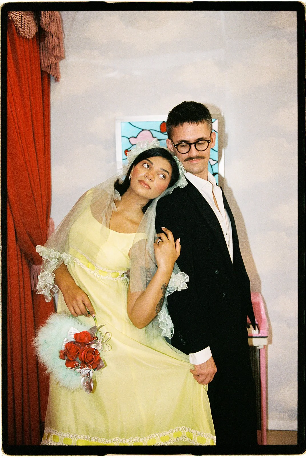 Couple posing together on 35mm film at Sure Thing NYC, with a pale yellow wedding dress, vintage veil, and red rose bouquet.