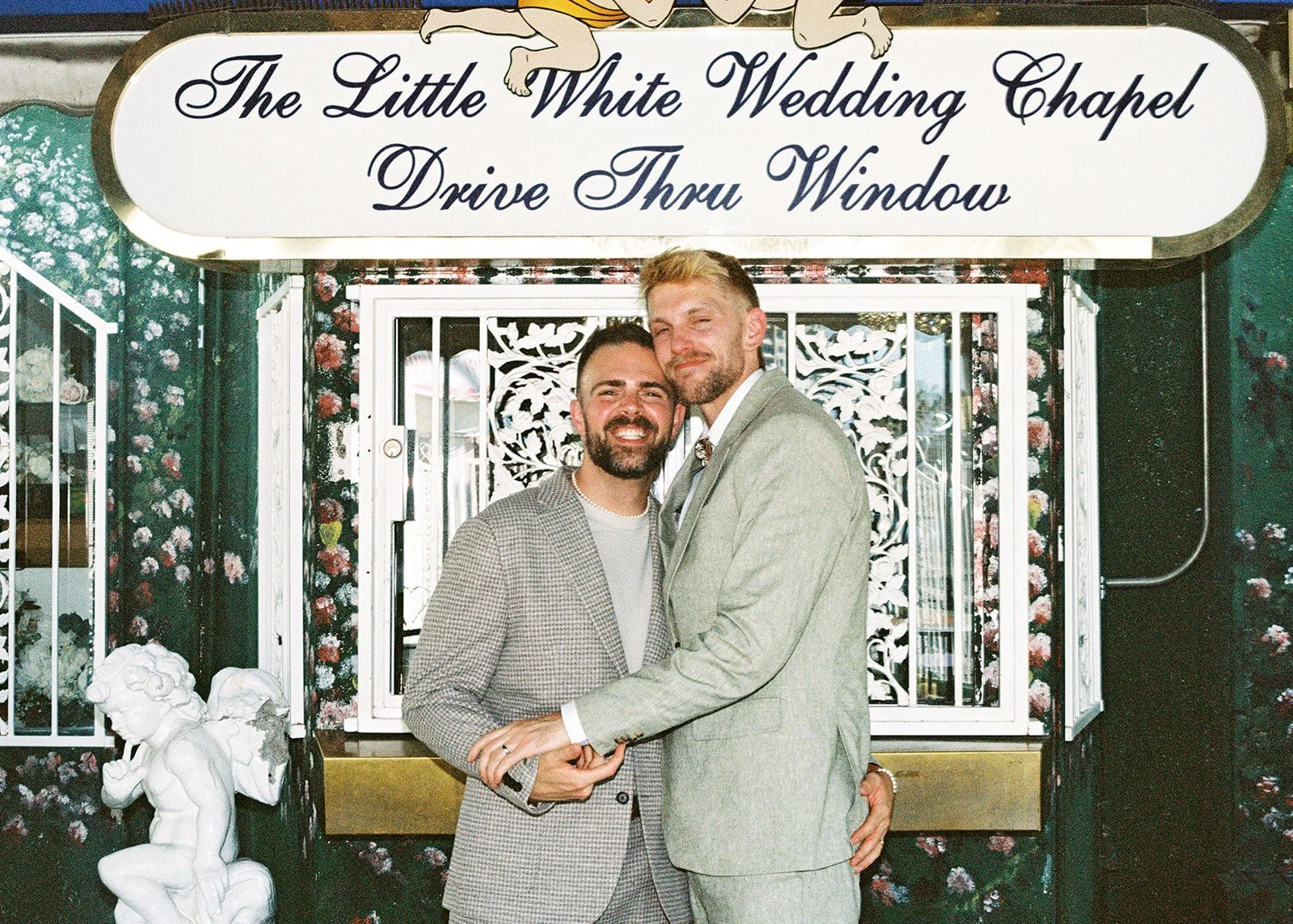 Couple smiling and hugging in front of the Littel White Wedding Chapels drive-thru window on 35mm film.