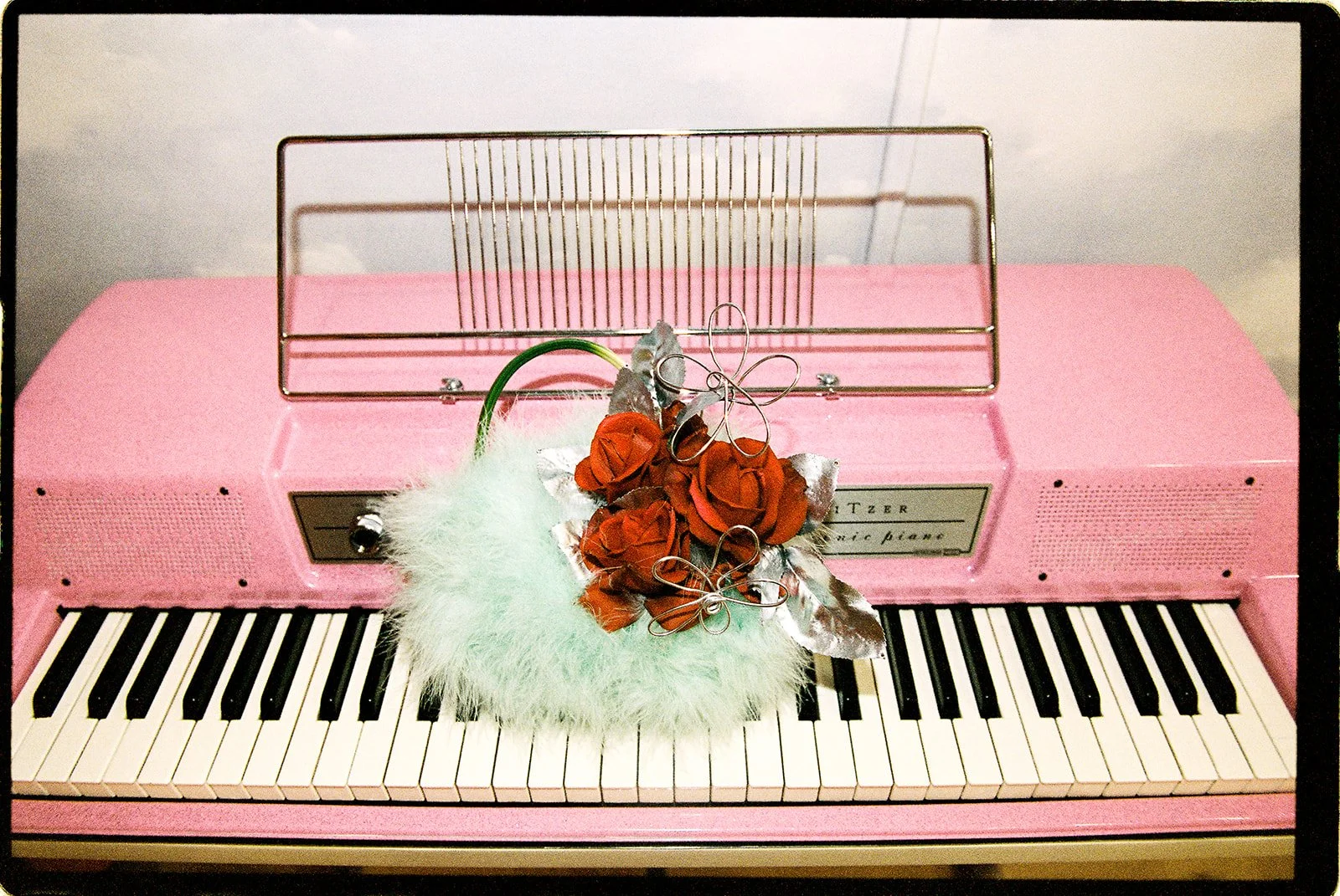 Red rose bridal bouquet with white feathers resting on a vintage pink Wurlitzer piano at Sure Thing NYC.