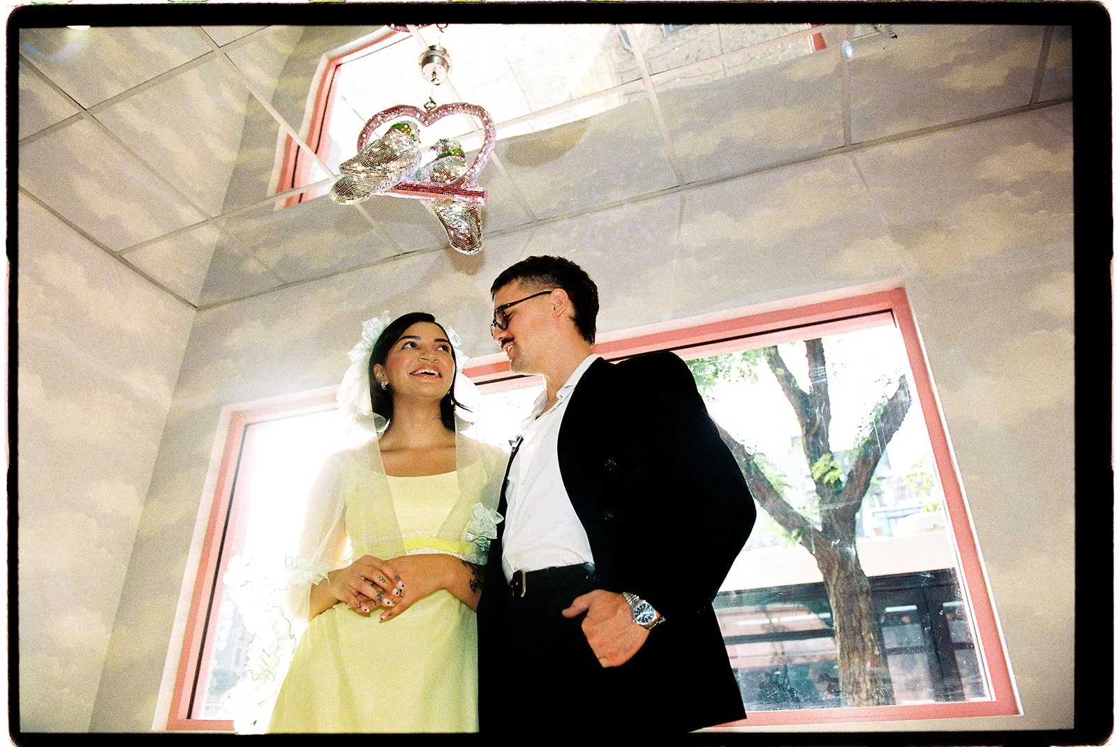 Low-angle 35mm film portrait of a couple beneath a mirrored ceiling and hanging silver bird decorations at Sure Thing NYC.