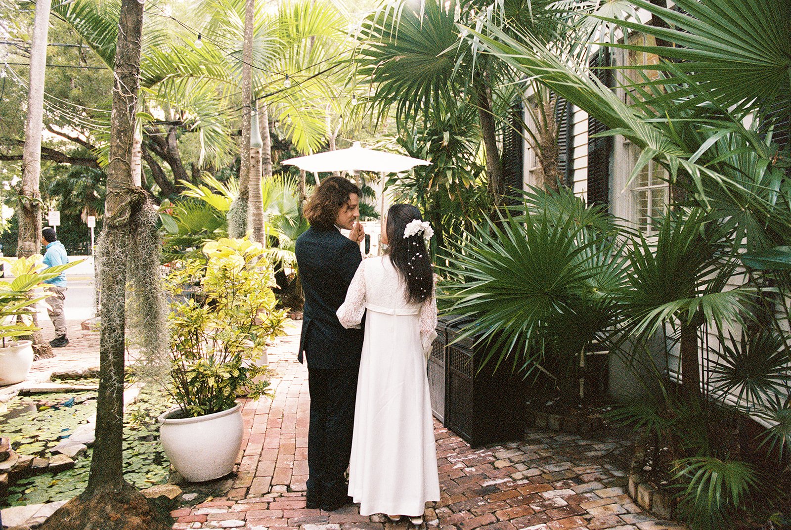 Bride and groom posing together under tropical palms outside Old Town Manor in Key West.