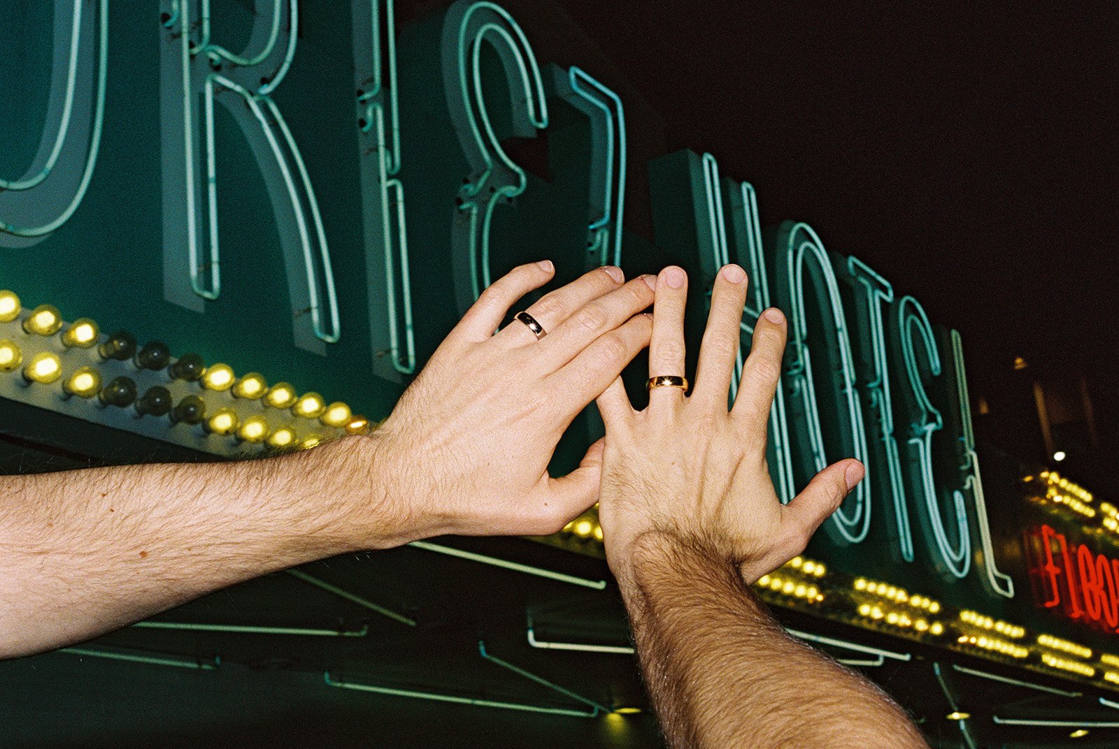 Couple holding their ring hands in the air during their nighttime Las Vegas Fremont Street elopement photos on 35mm film.