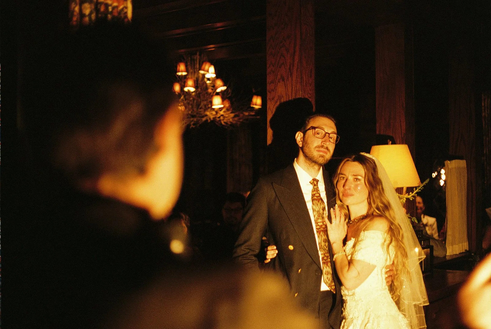Moody film wedding portrait of the bride and groom standing together inside the warmly lit Deer Mountain Inn reception.