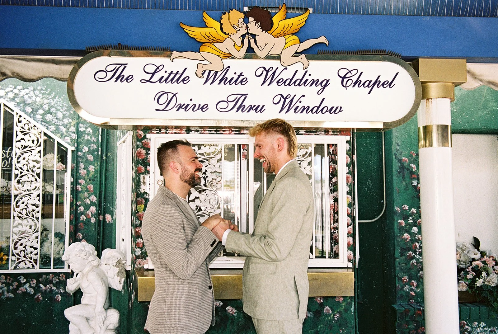 Couple holding hands in front of the Little White Wedding Chapels drive-thru window for their Las Vegas elopement on 35mm film.