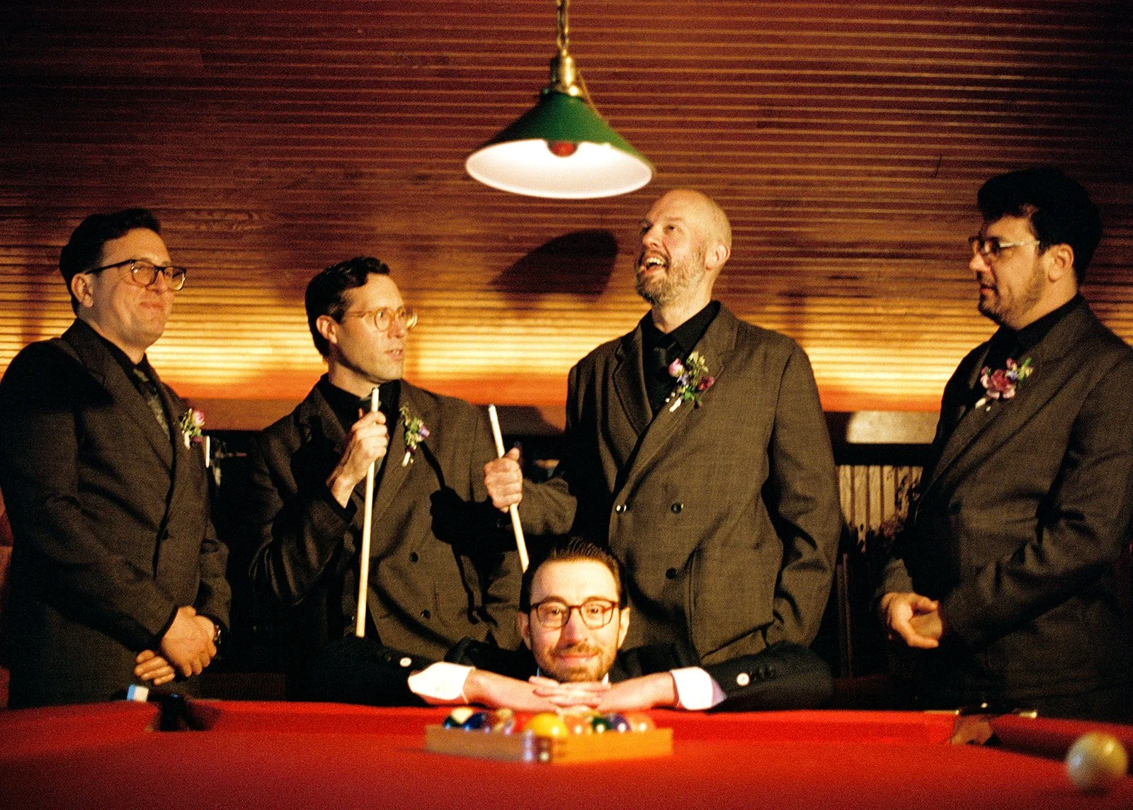 Candid film photo of the groom and groomsmen laughing and posing around the pool table before the wedding.