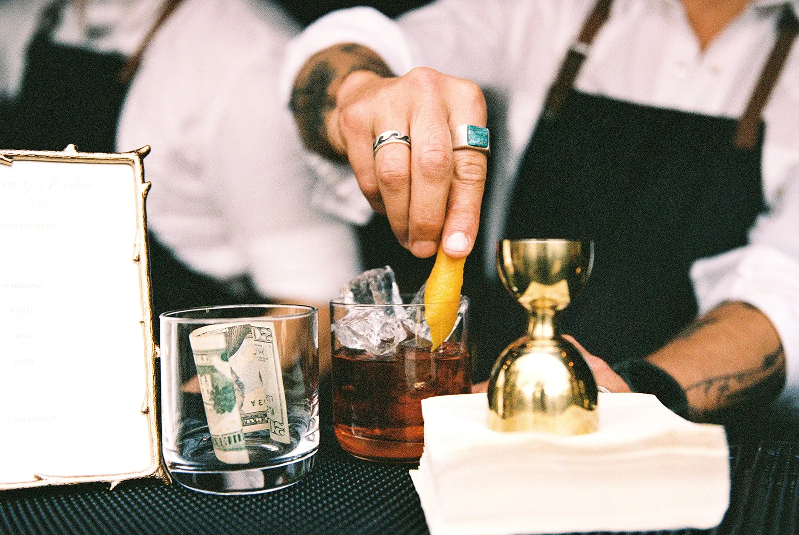 Film detail photo of a bartender adding an orange peel garnish to a cocktail at Deer Mountain Inn.