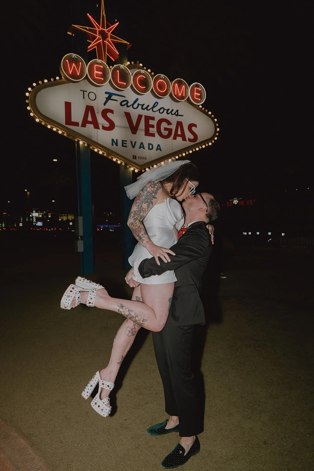 Bride and groom sharing a kiss beneath the Welcome to Fabulous Las Vegas sign during nighttime wedding portraits.