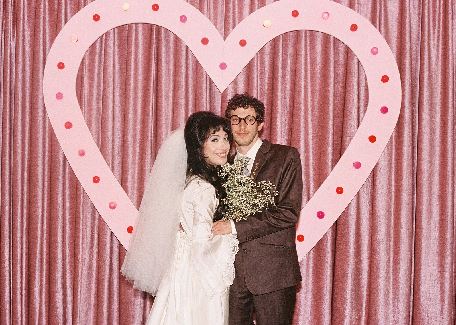 Bride and groom posing in front of the pink Sure Thing heart for their vintage Vegas wedding photos.