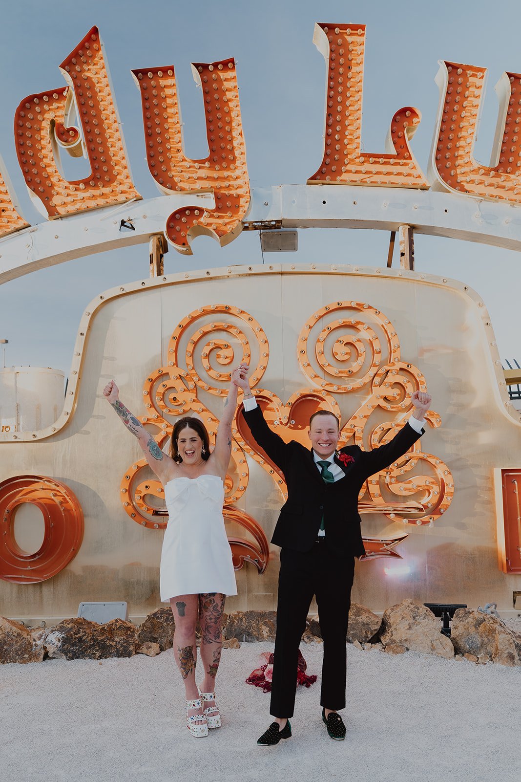 Bride and groom raising their arms in celebration after their Neon Museum Las Vegas wedding ceremony.