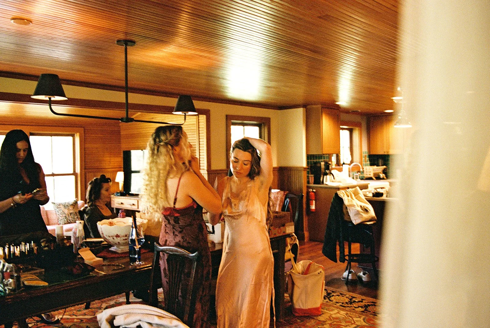 Candid film photo of the bride having her hair styled while getting ready with friends inside the Tuckaway cottage.